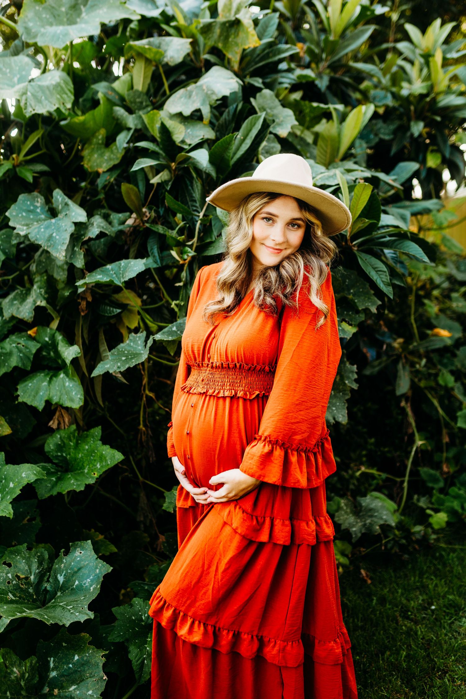 a pregnant mom in orange holds her belly and softly smiles at the camera