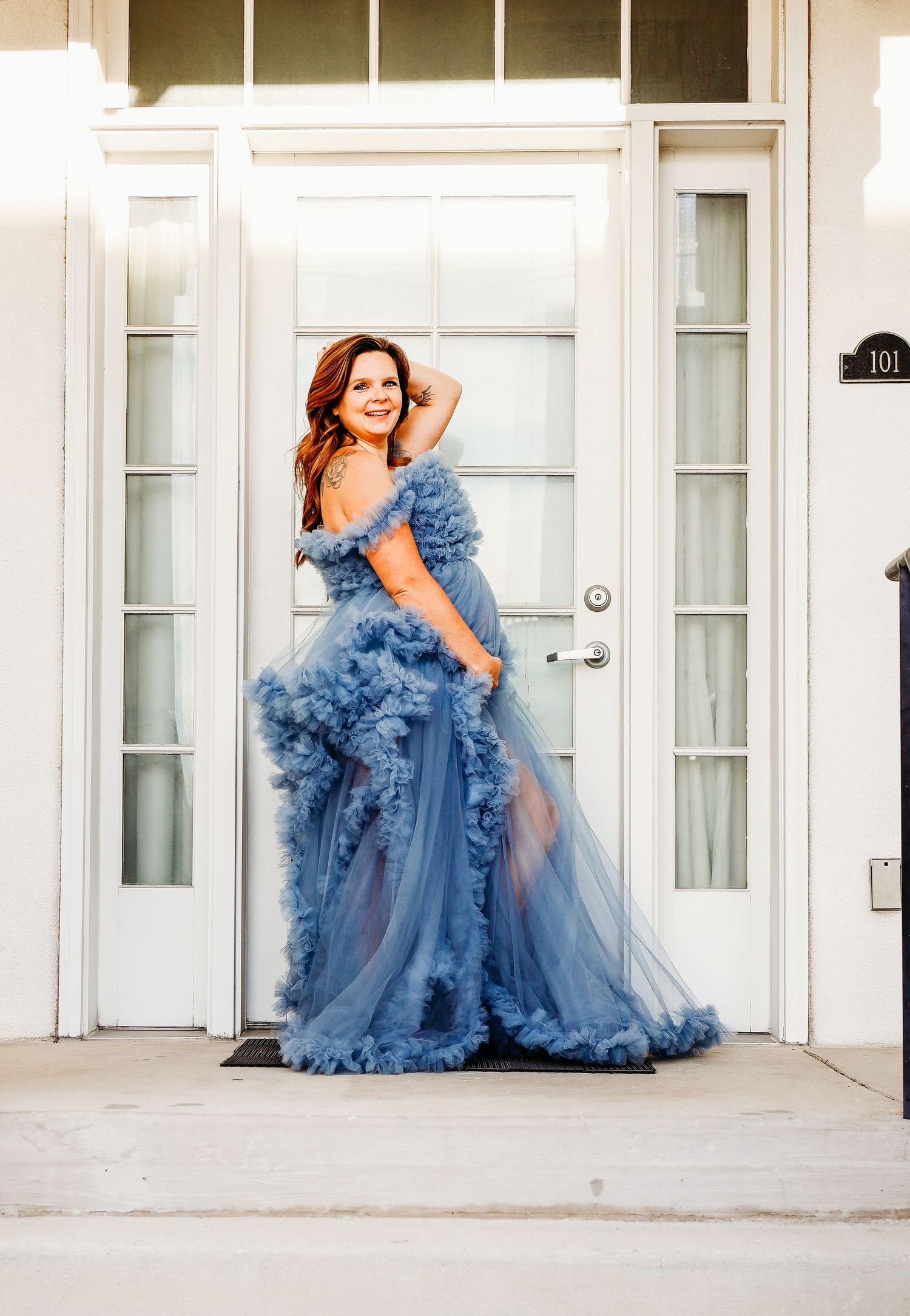 a pregnant mother in a big blue dress holds her belly and smiles