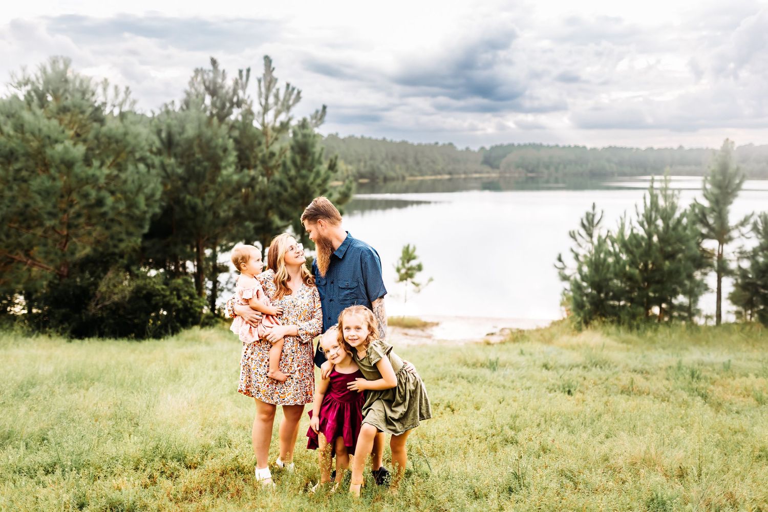 two parents smile at each other with their three daughters in front of smith creek park lake