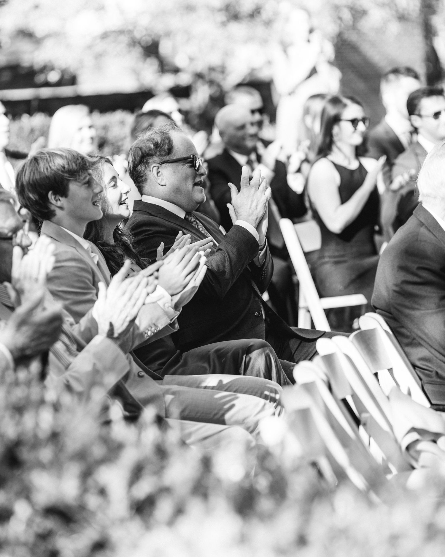 Black and white photo of audience members clapping and applauding outdoors.