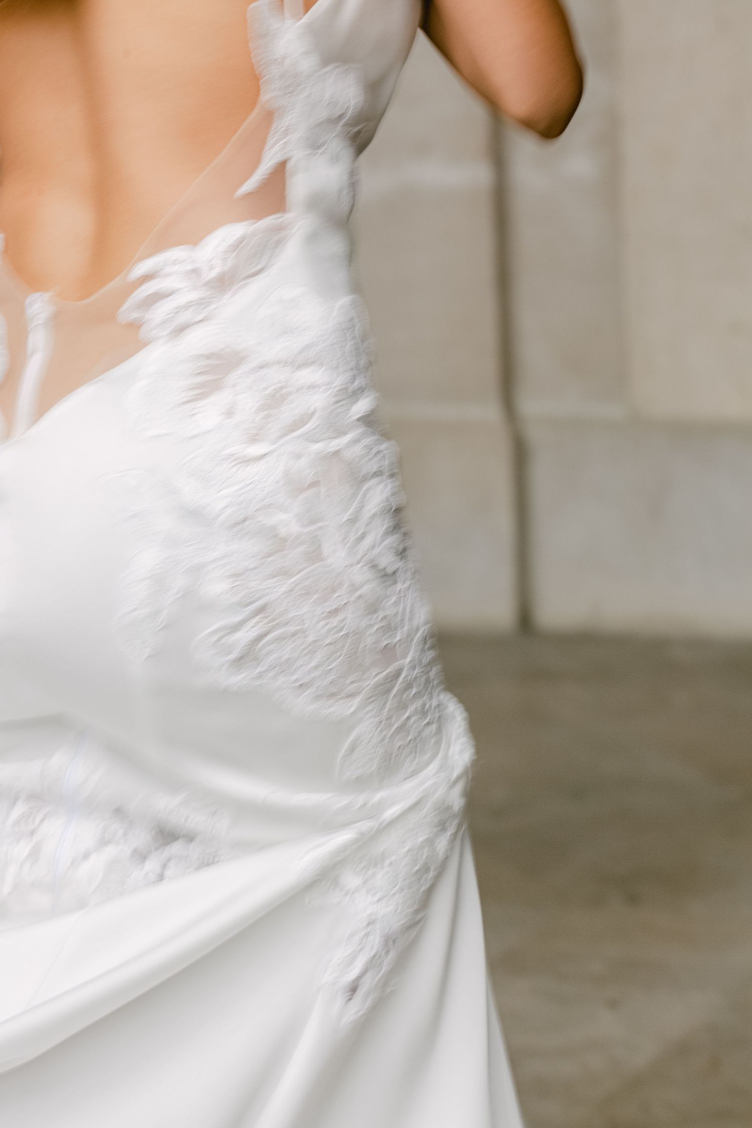 Close-up detail of white feathered wedding dress with delicate texture and movement against neutral background.