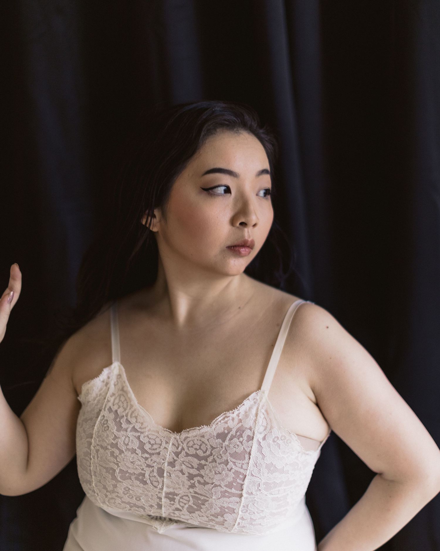Figure in a delicate white lace camisole poses against a dark background with dramatic lighting.