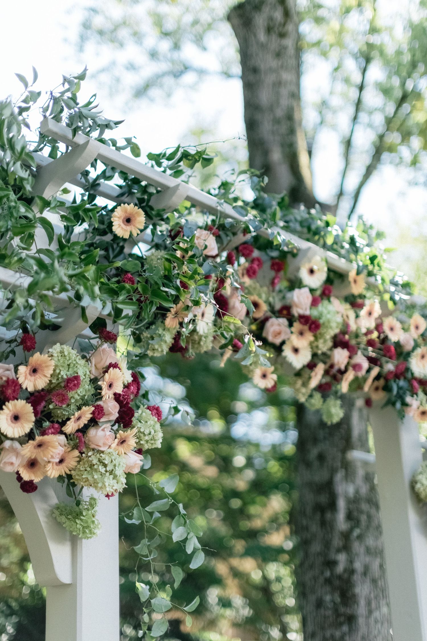 Close-up of floral arch with pink and burgundy blooms against green foliage.