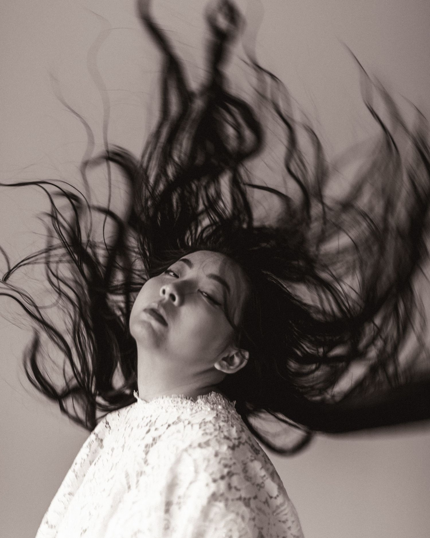 Dramatic black and white portrait featuring flowing dark hair spread out against light background in artistic motion.