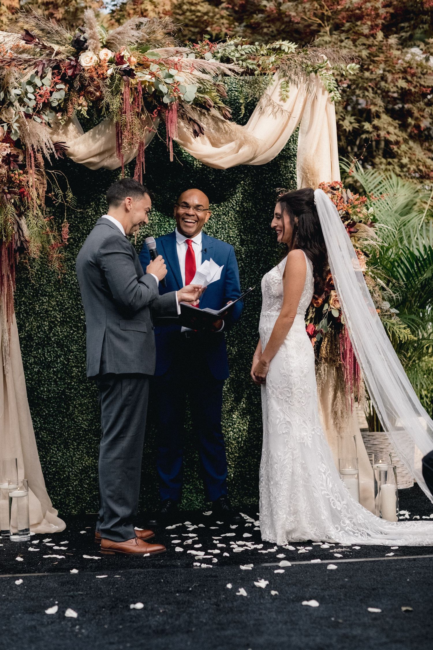Wedding ceremony under a draped floral arch with gorgeous dried flowers and white fabric.