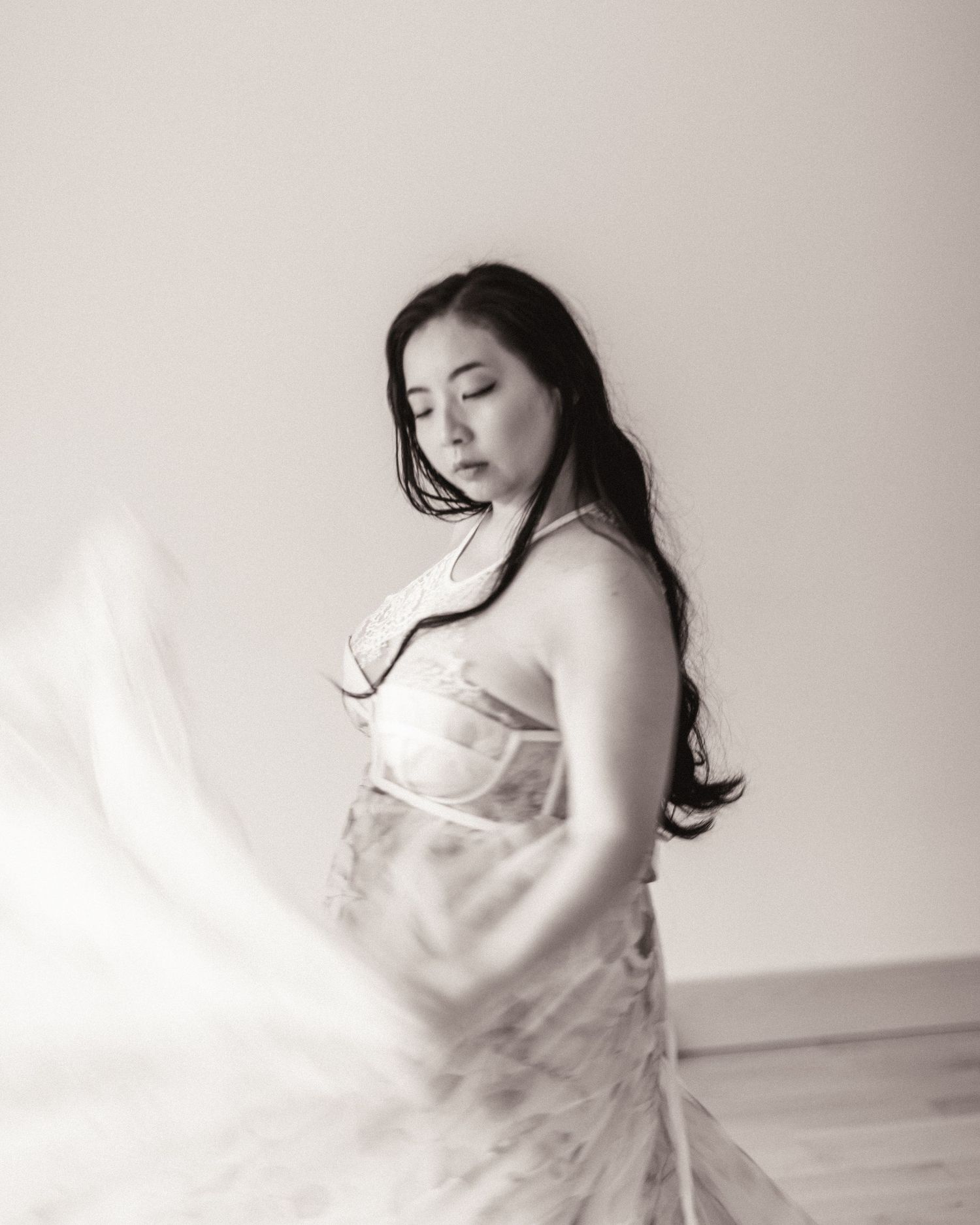 Black and white artistic portrait of someone in a flowing dress posing gracefully against a minimal background.