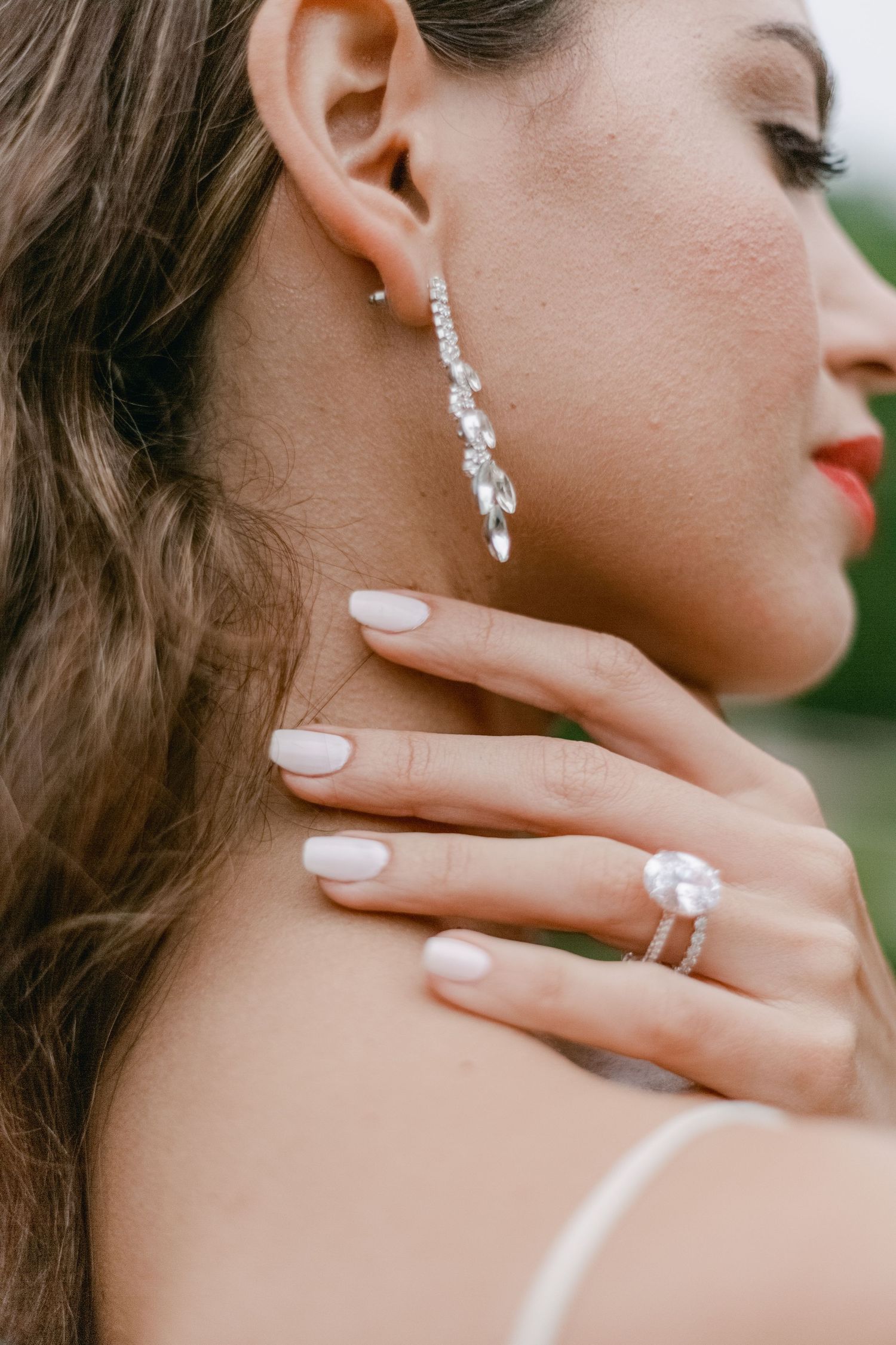 Close-up of elegant bridal jewelry showing sparkling diamond drop earrings and engagement ring with neutral manicure.