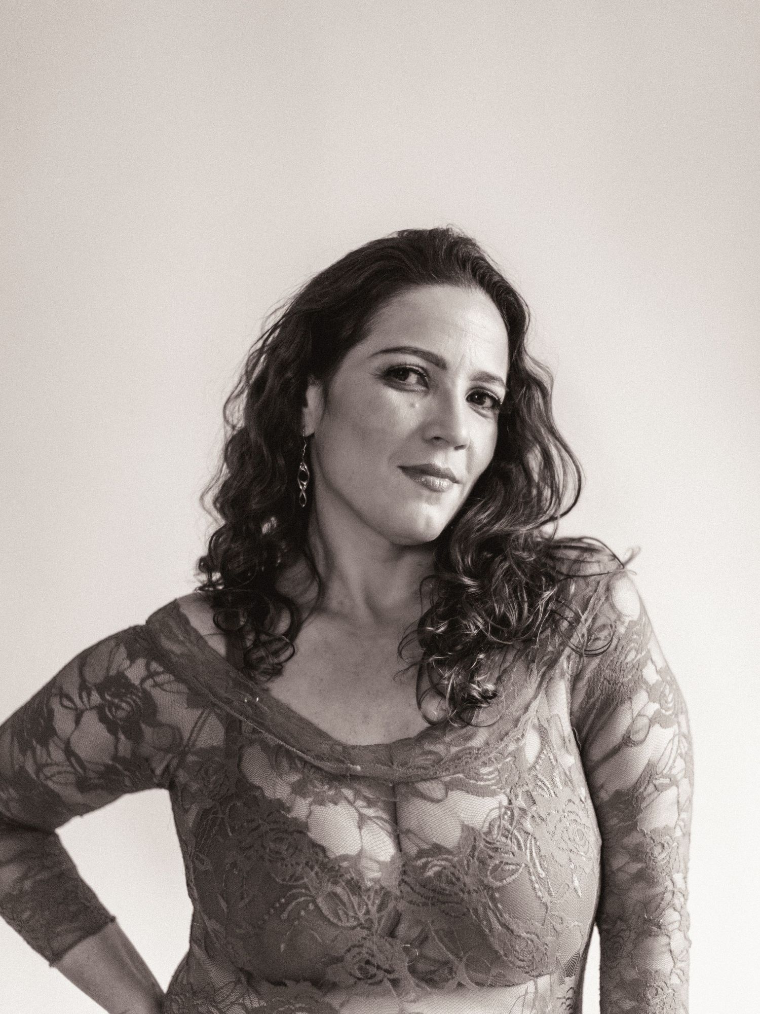 A black and white portrait shows a woman with dark curly hair wearing a delicate lace top against a plain background.