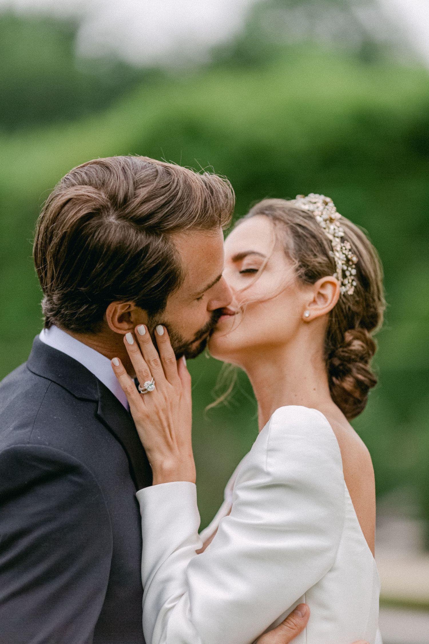 Romantic wedding portrait with couple sharing intimate kiss, bride wearing white dress and floral hairpiece, groom in dark suit.