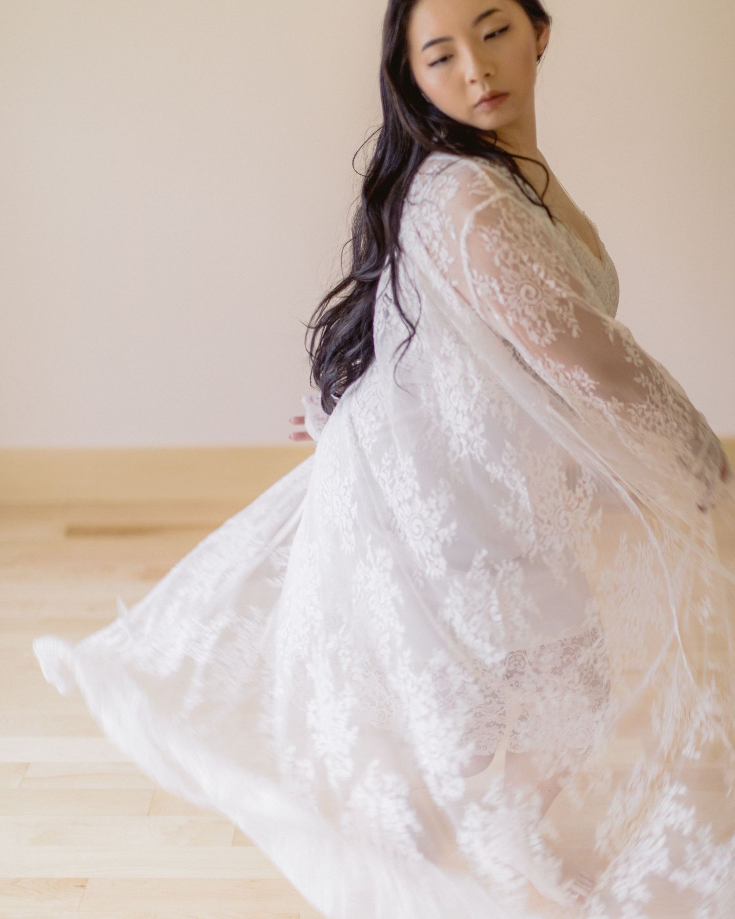 Graceful portrait in flowing white lace dress twirling against minimal beige background.