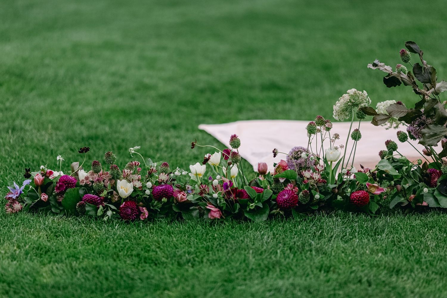 Pink and purple flowers border a white bathtub set in lush green grass in an outdoor garden setting.