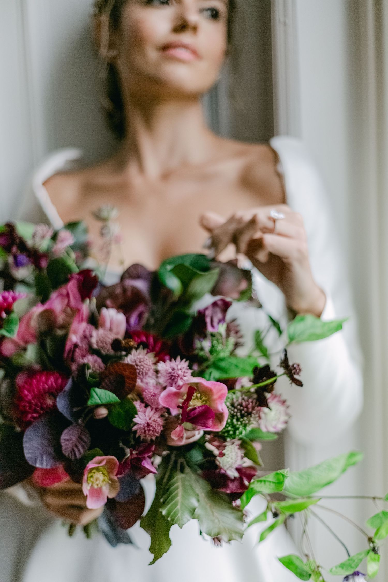 Beautiful bridal bouquet features rich burgundy and pink blooms with lush greenery against a white wedding dress background.