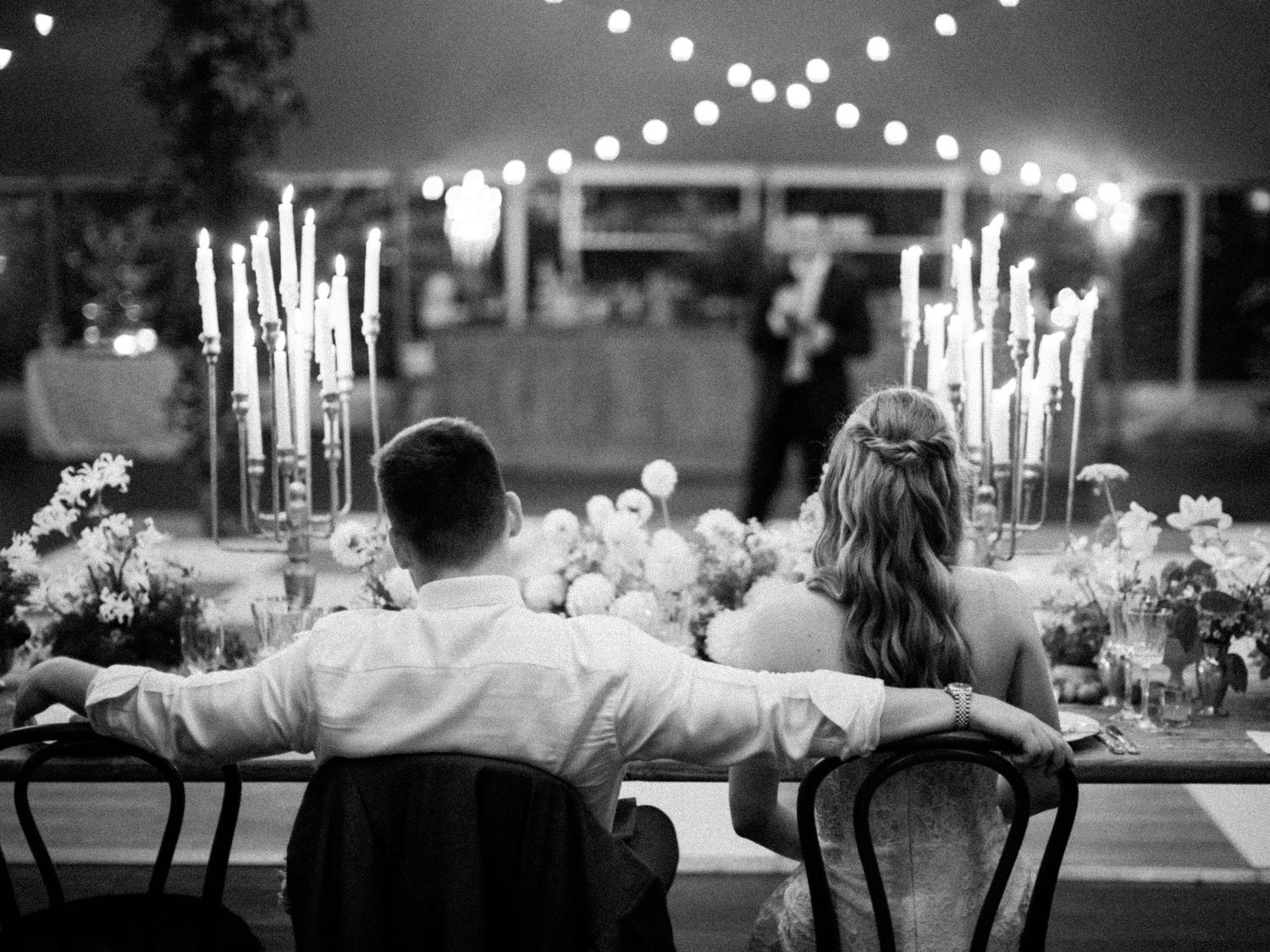 Black and white wedding reception table settings with glowing candles and string lights creating an elegant ambiance.