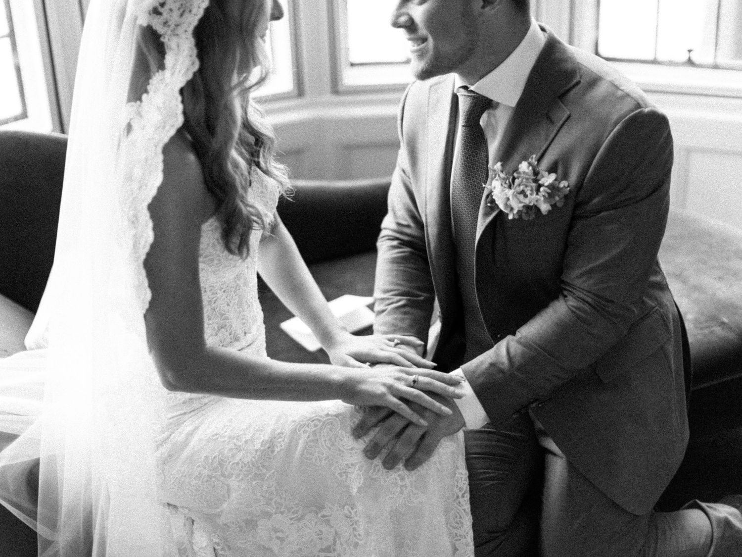 Black and white moment of couple holding hands on vintage sofa during wedding.