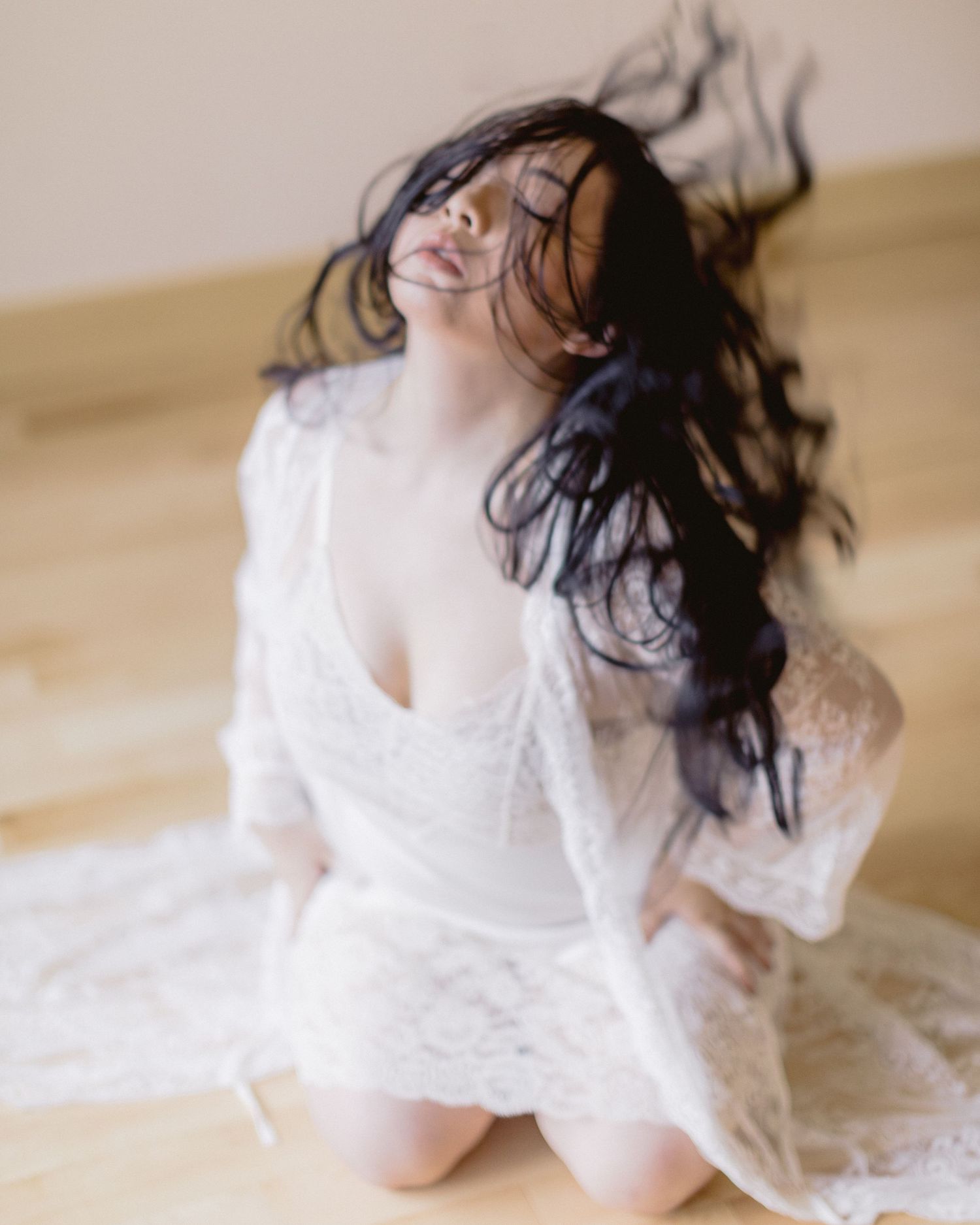 A person wearing a white lace dress sits on a floor while their dark hair flows in motion.