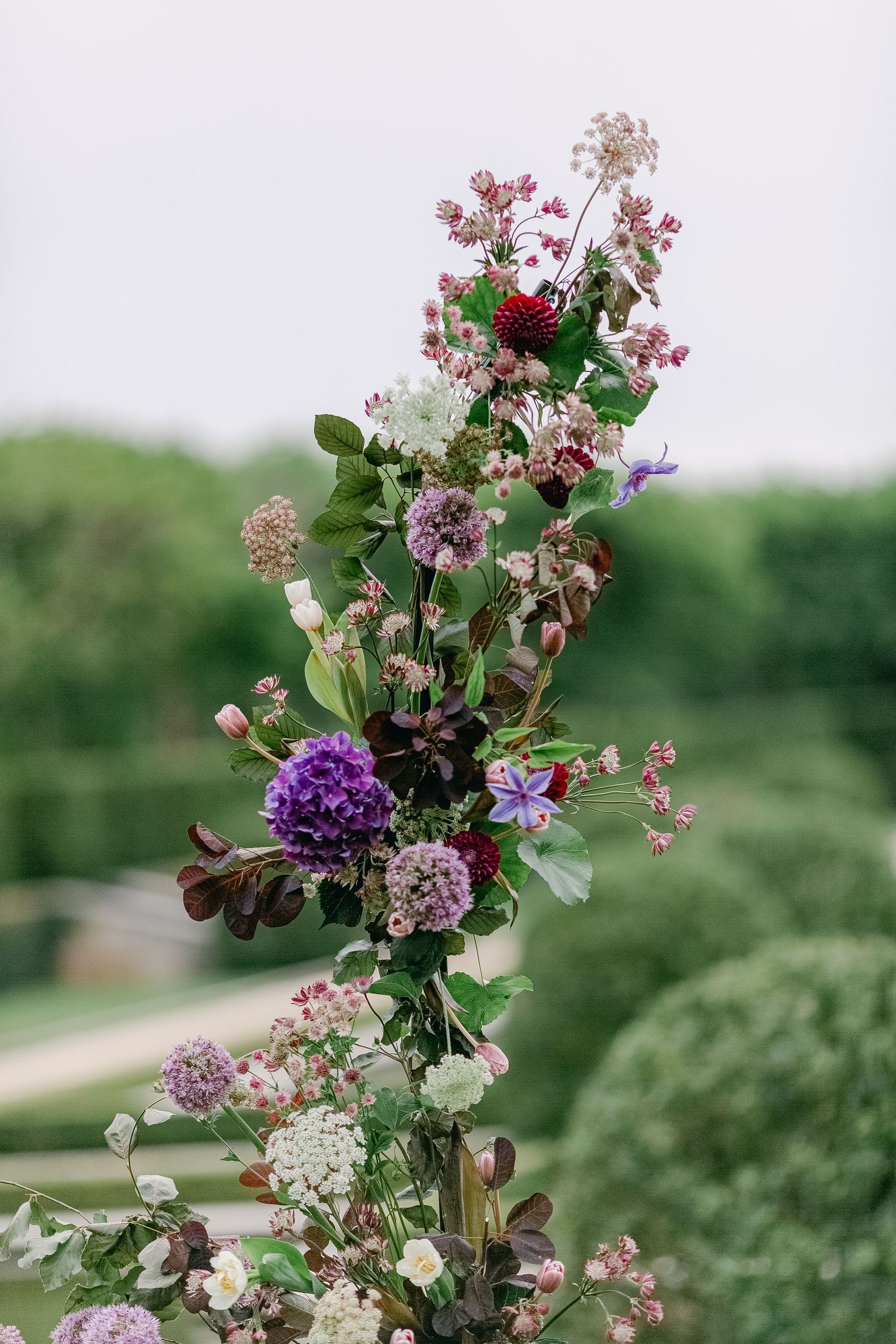 Beautiful floral arrangement featuring purple alliums, pink blossoms, and delicate white flowers against a blurred green backdrop.