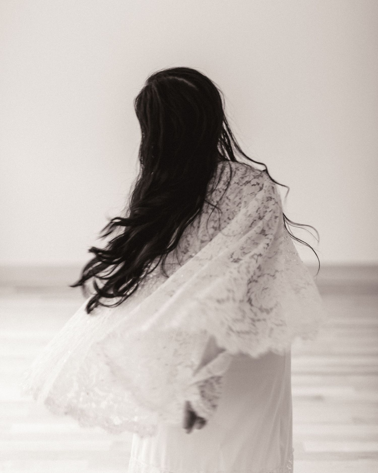 A silhouetted figure in a white flowy dress with long dark hair stands against a soft, dreamy background.