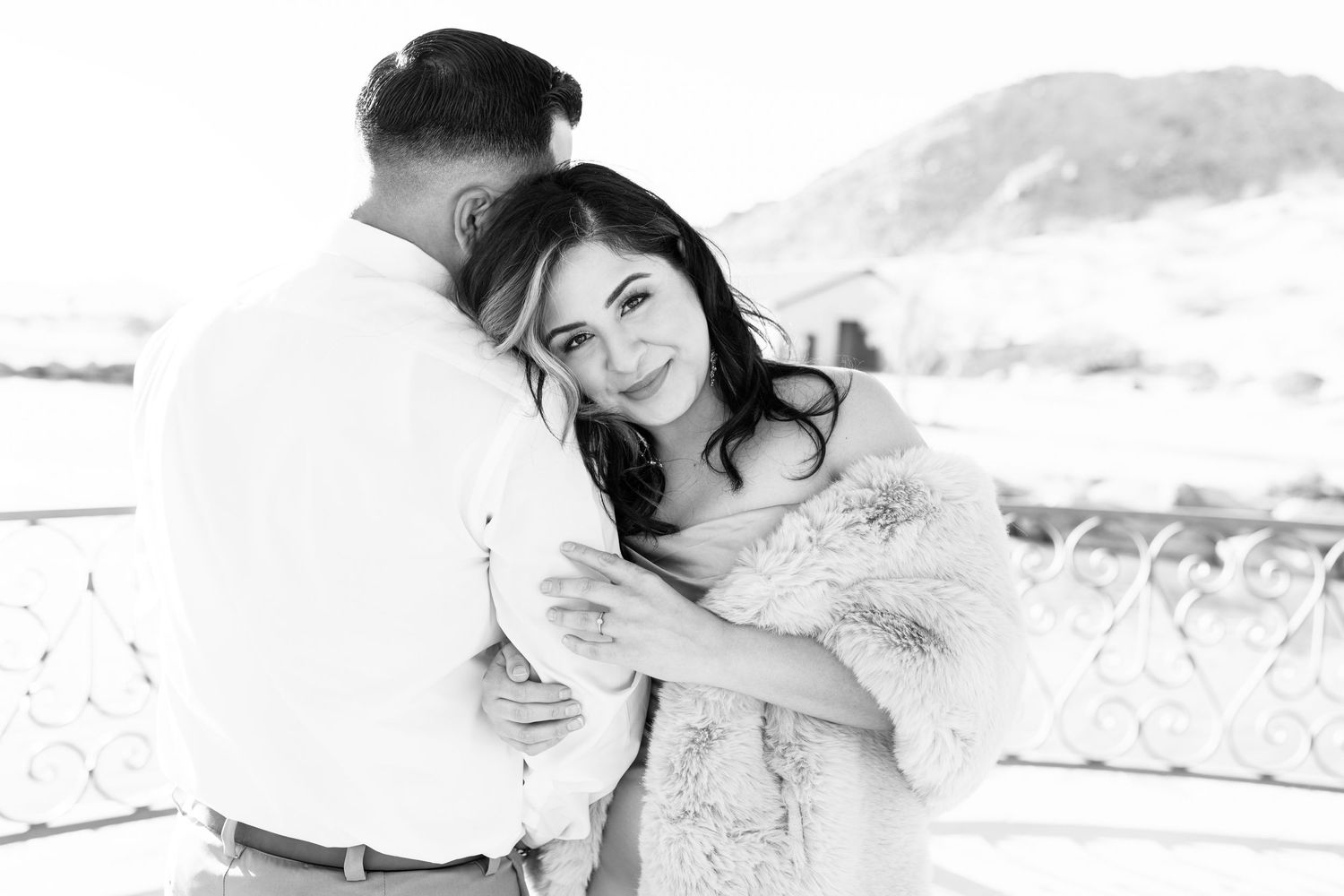 Black and white image of a husband facing in a slightly v shape back to me while the wifes head lays on his shoulder facing me