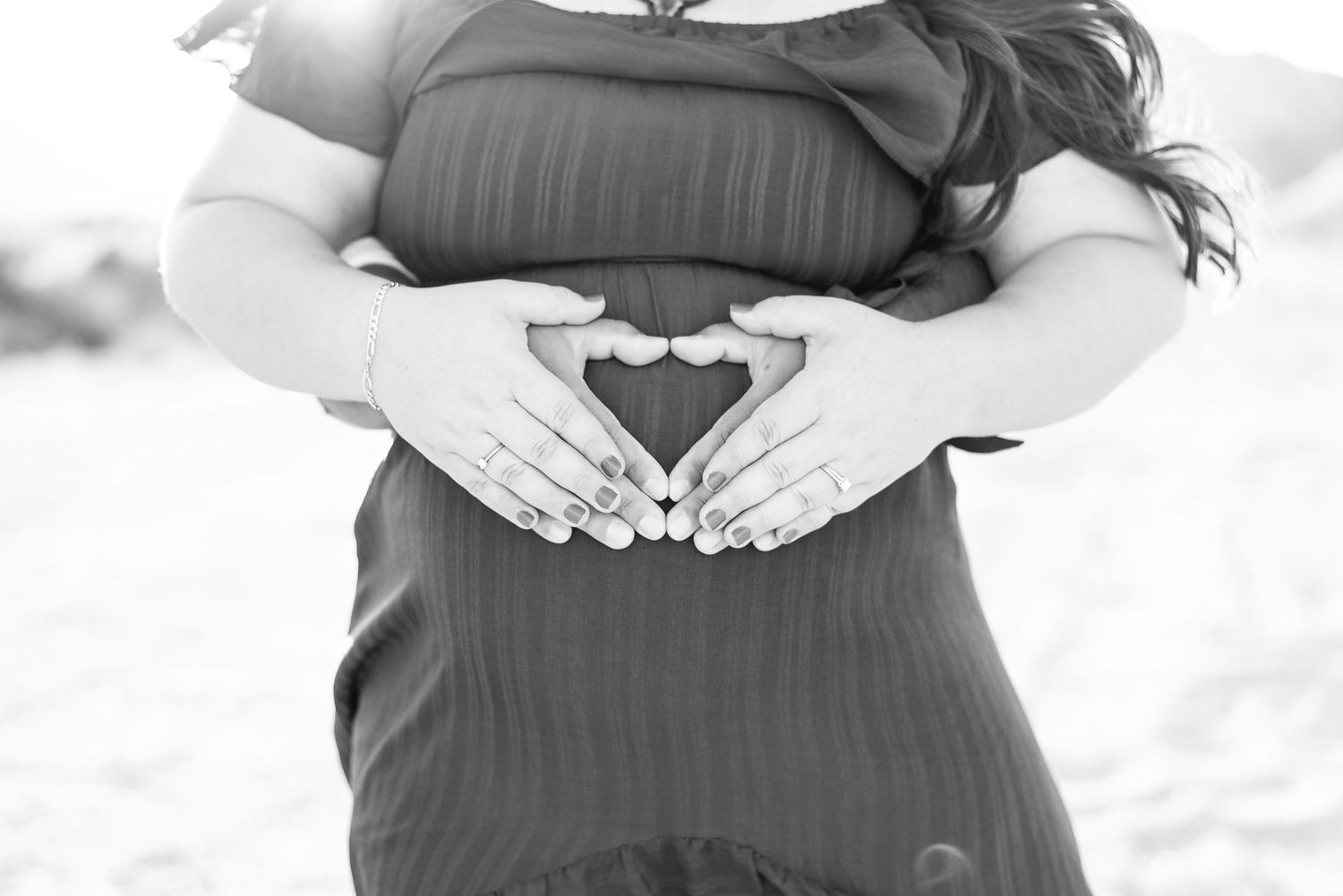 zoomed in black and white image of a soon to be mothers belly with dads hands on the belly creating a heart shape with moms hands on his