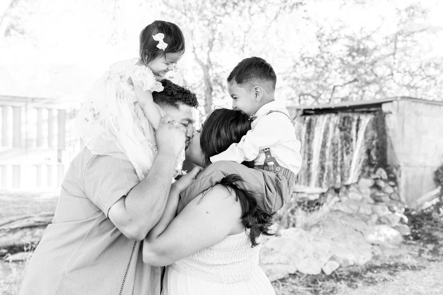 mom and dad holding one child on their shoulders as they're leaning in for a little smooch while both children look down at them smiling big
