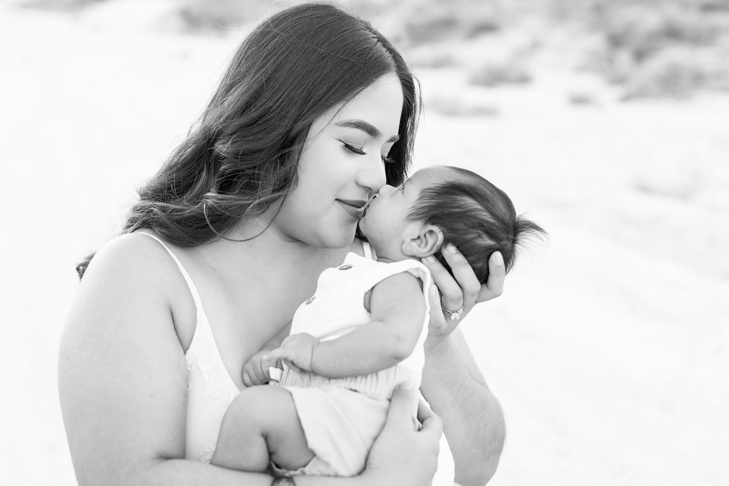 black and white image of zoomed in slightly side profile of a mother and her newborn son as she holds him in her arms as they touch noses