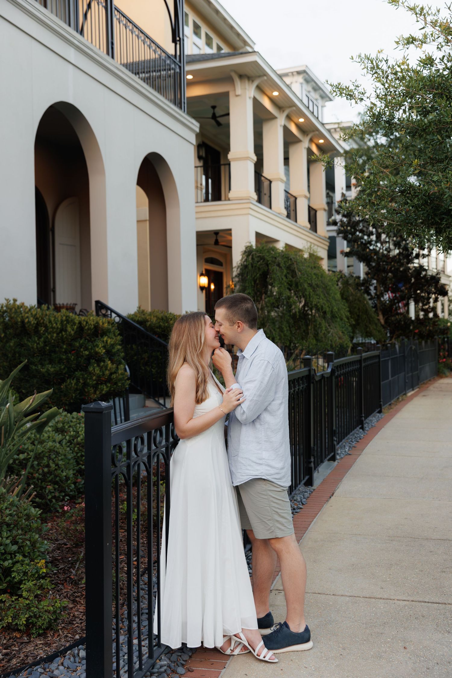 Couple sharing a romantic moment on a sidewalk outside an elegant white building with arched details.