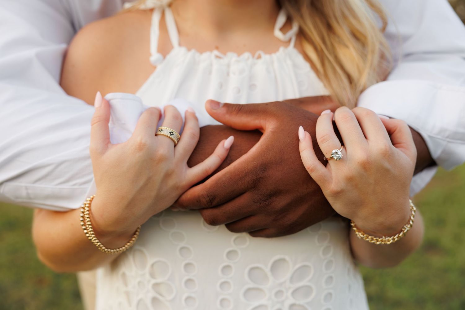 Close-up of an interracial couple embracing, showcasing engagement ring and gold bracelets on woman's hands.