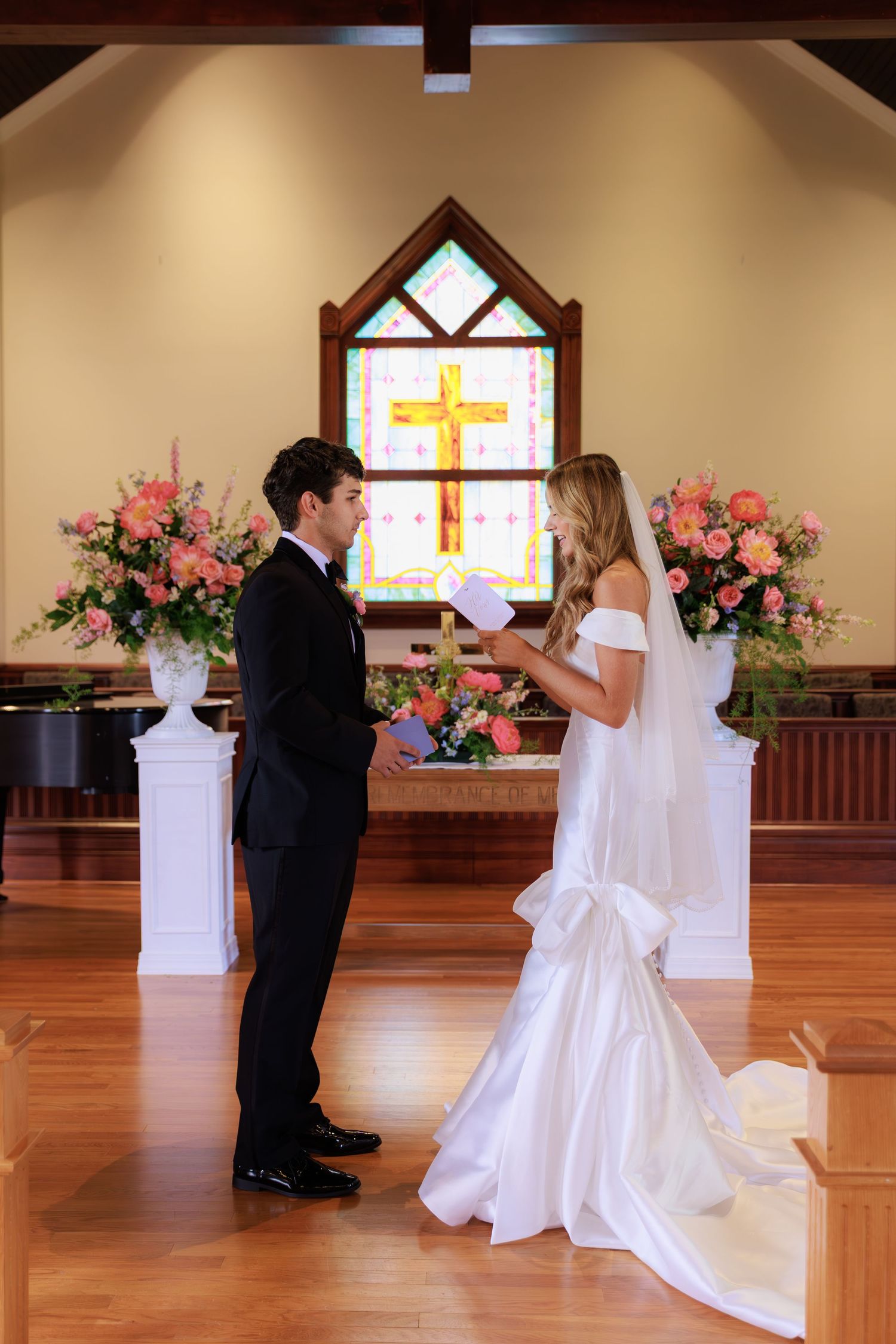 A wedding ceremony first look moment with bride in white dress and groom in black suit in a church with pink floral decor.