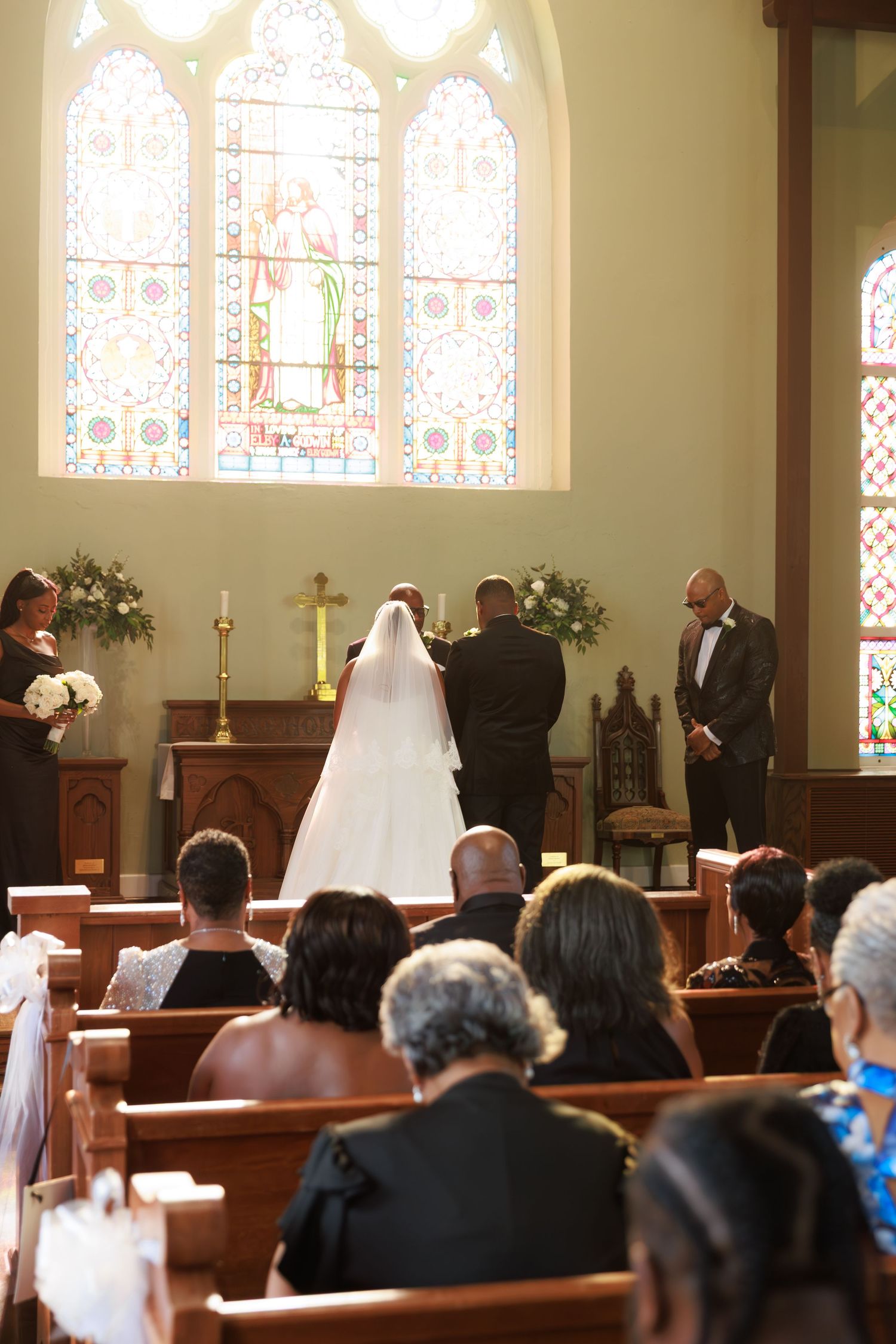 Wedding ceremony taking place in a traditional church with stained glass windows and wooden pews filled with guests.