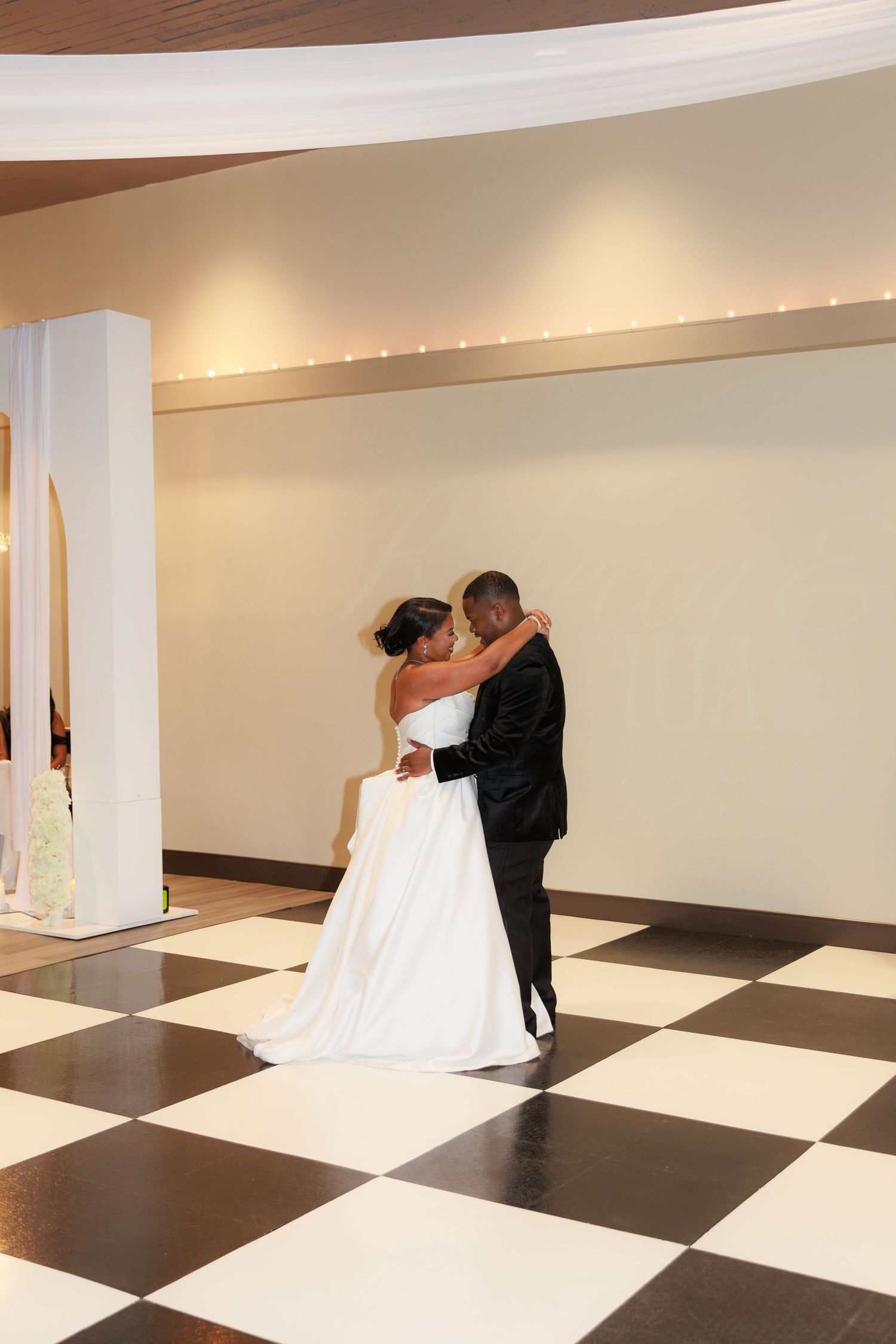 A bride and groom share an intimate dance on a black and white checkered ballroom floor.