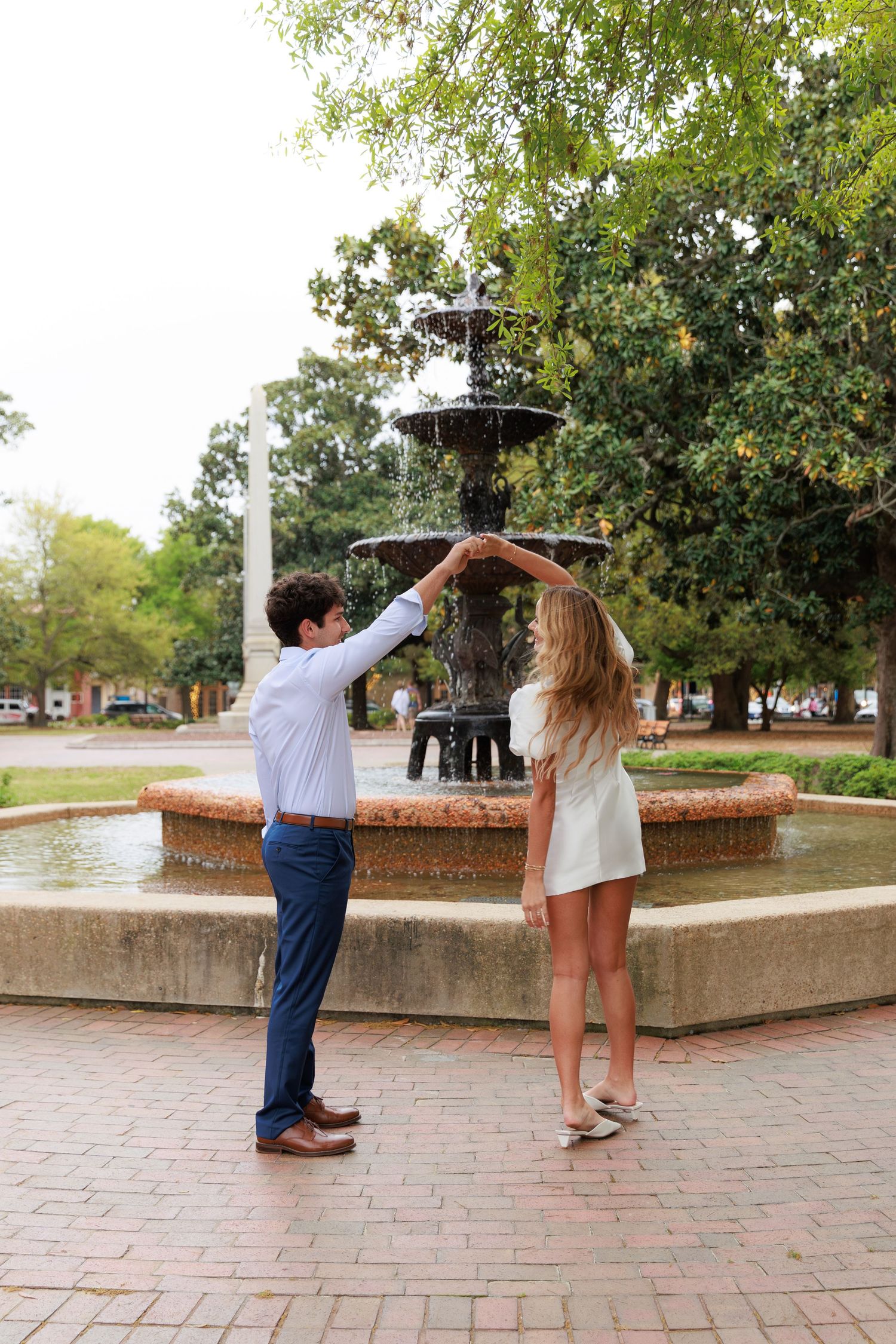 Two people dancing together on a brick patio surrounded by trees and landscaping in a romantic moment.
