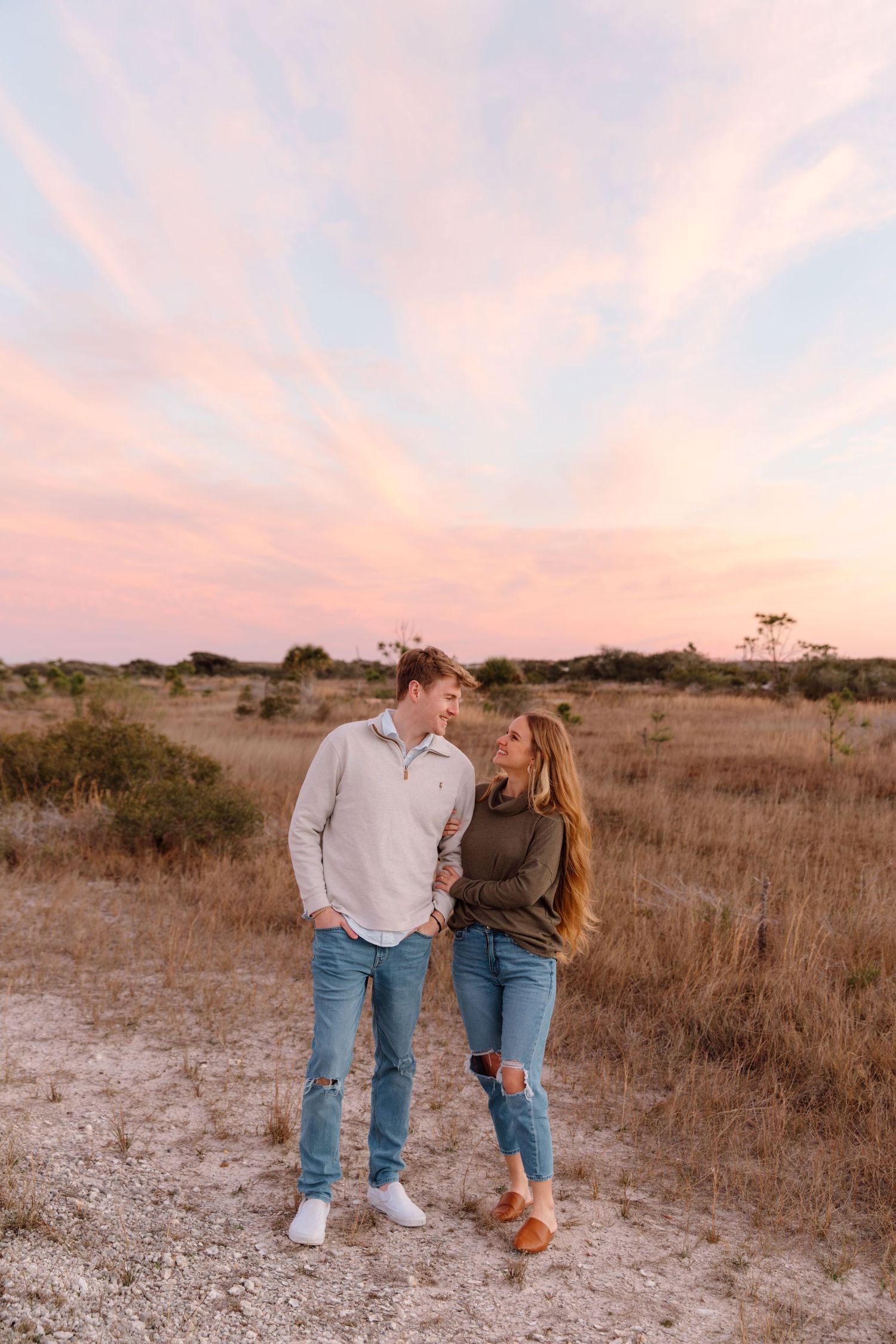 Couple in casual denim outfits sharing a romantic moment in an open field at sunset.