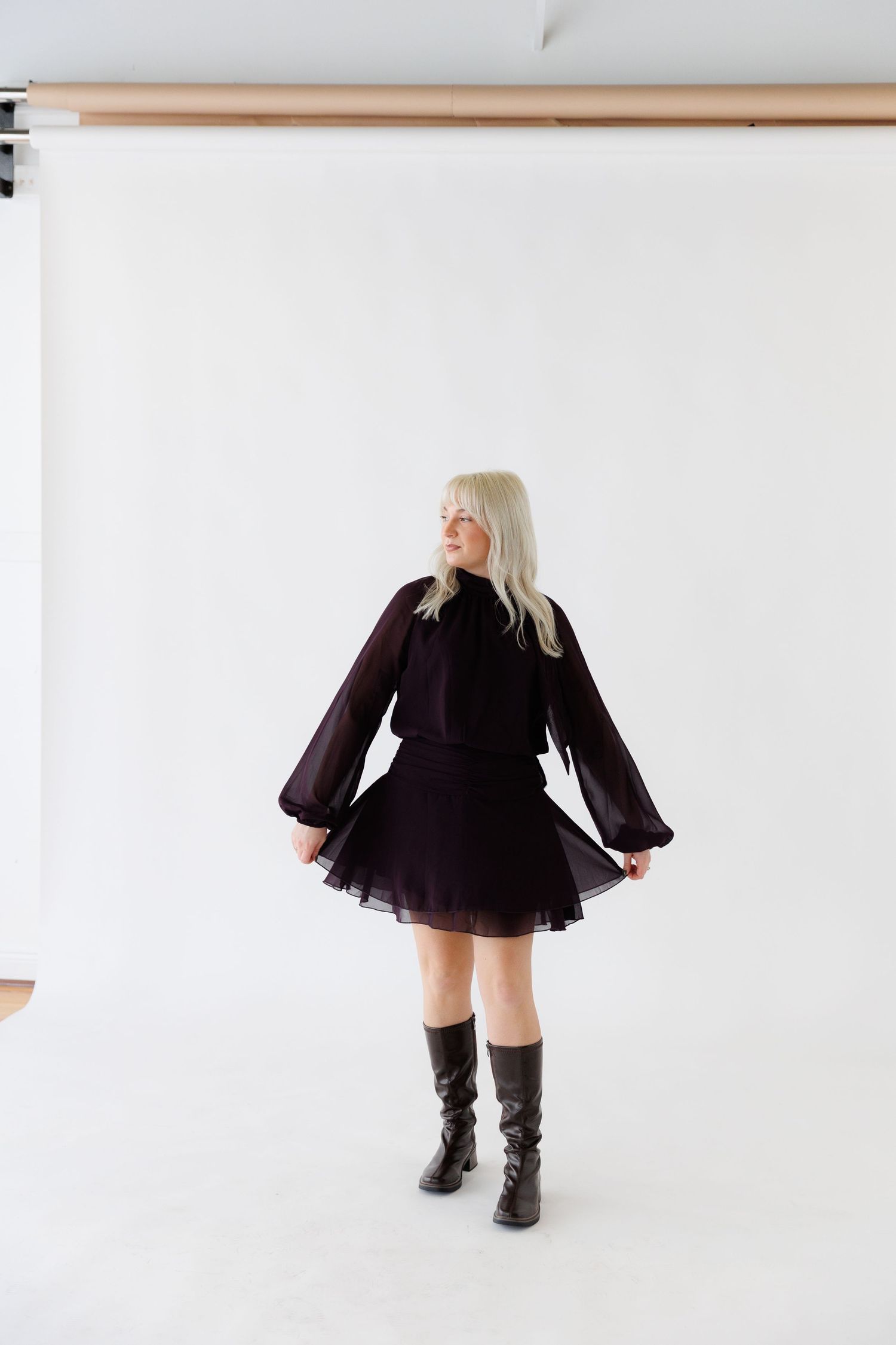 Person in purple dress and boots twirling against white studio backdrop.