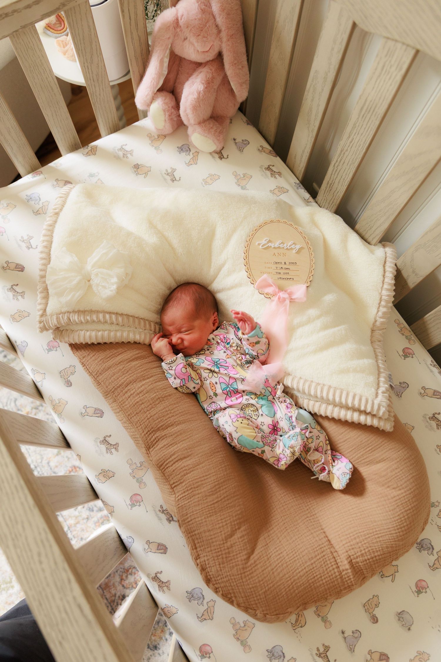 A cozy nursery crib with floral bedding, plush toys, and soft textiles in neutral and pink tones.