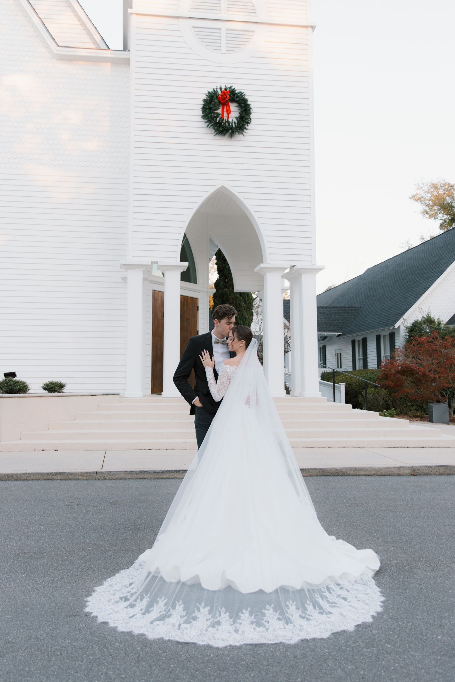 Classic white church wedding scene with Christmas wreath and flowing bridal train.