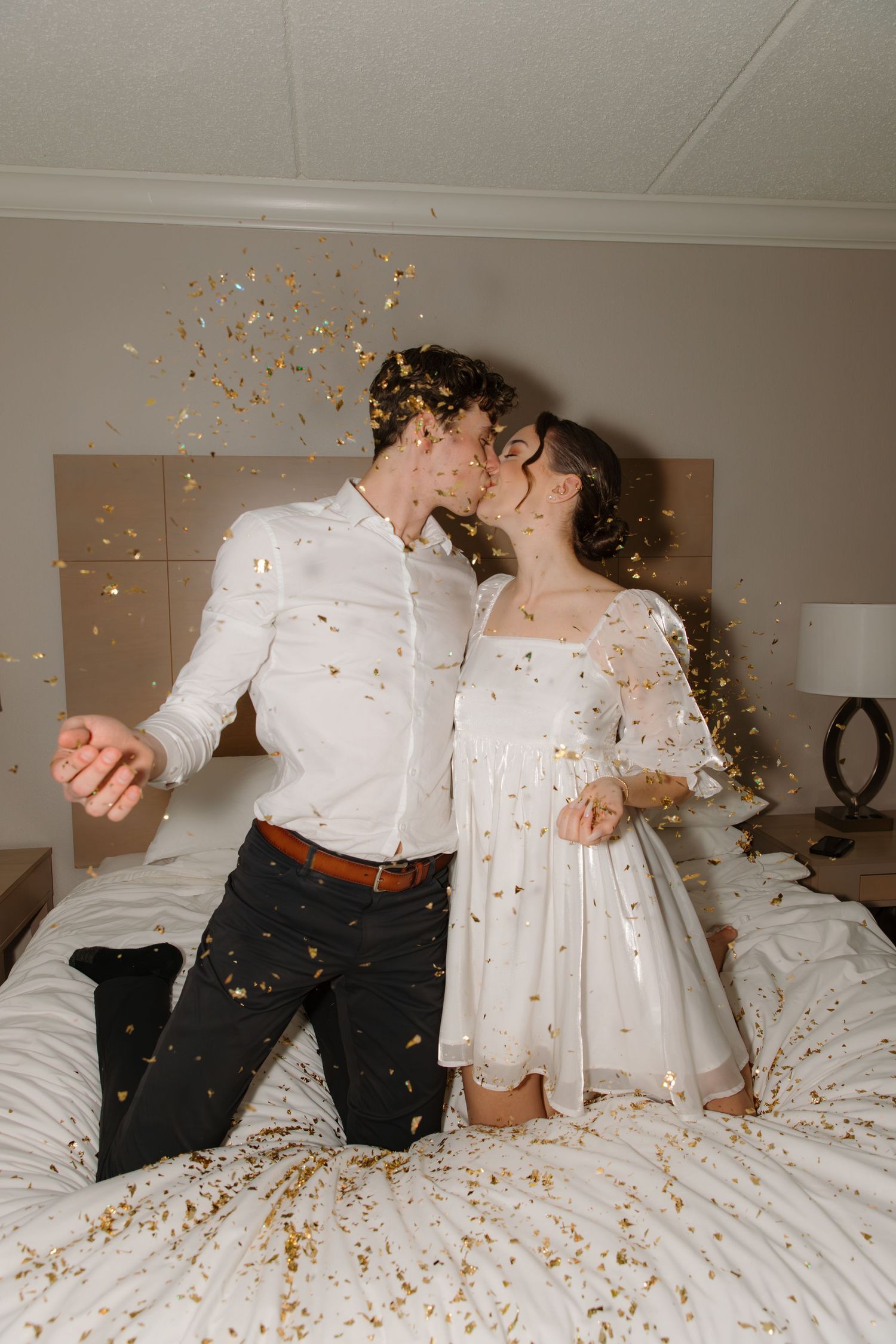 Couple lying on bed while gold confetti rains down in romantic celebration sequence.