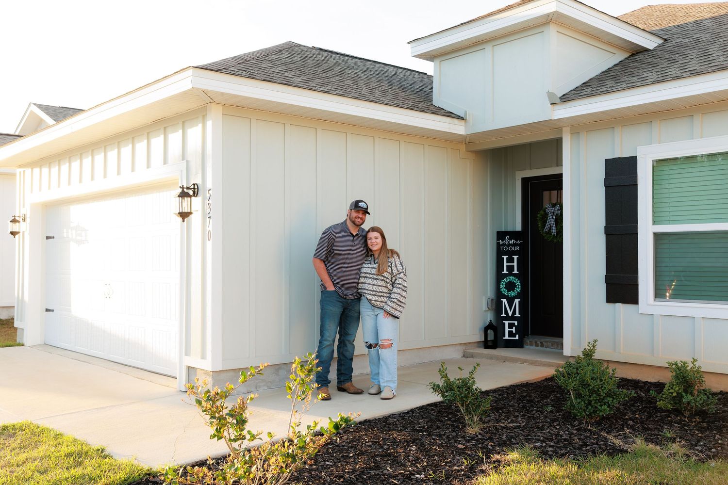 People standing outside a white residential home with landscaping and a front door entrance.
