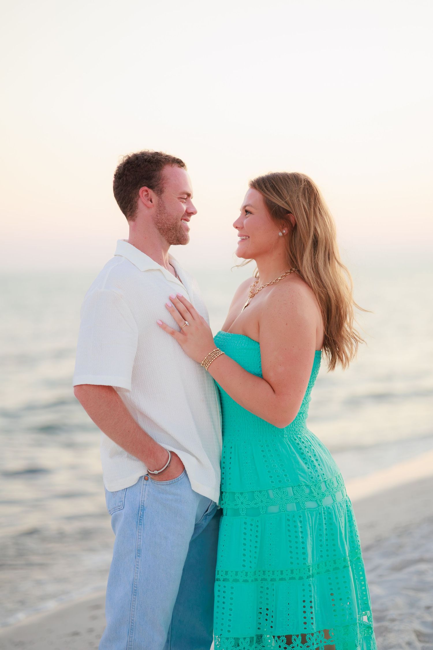 A couple in beachwear shares a romantic moment along the shoreline at sunset.