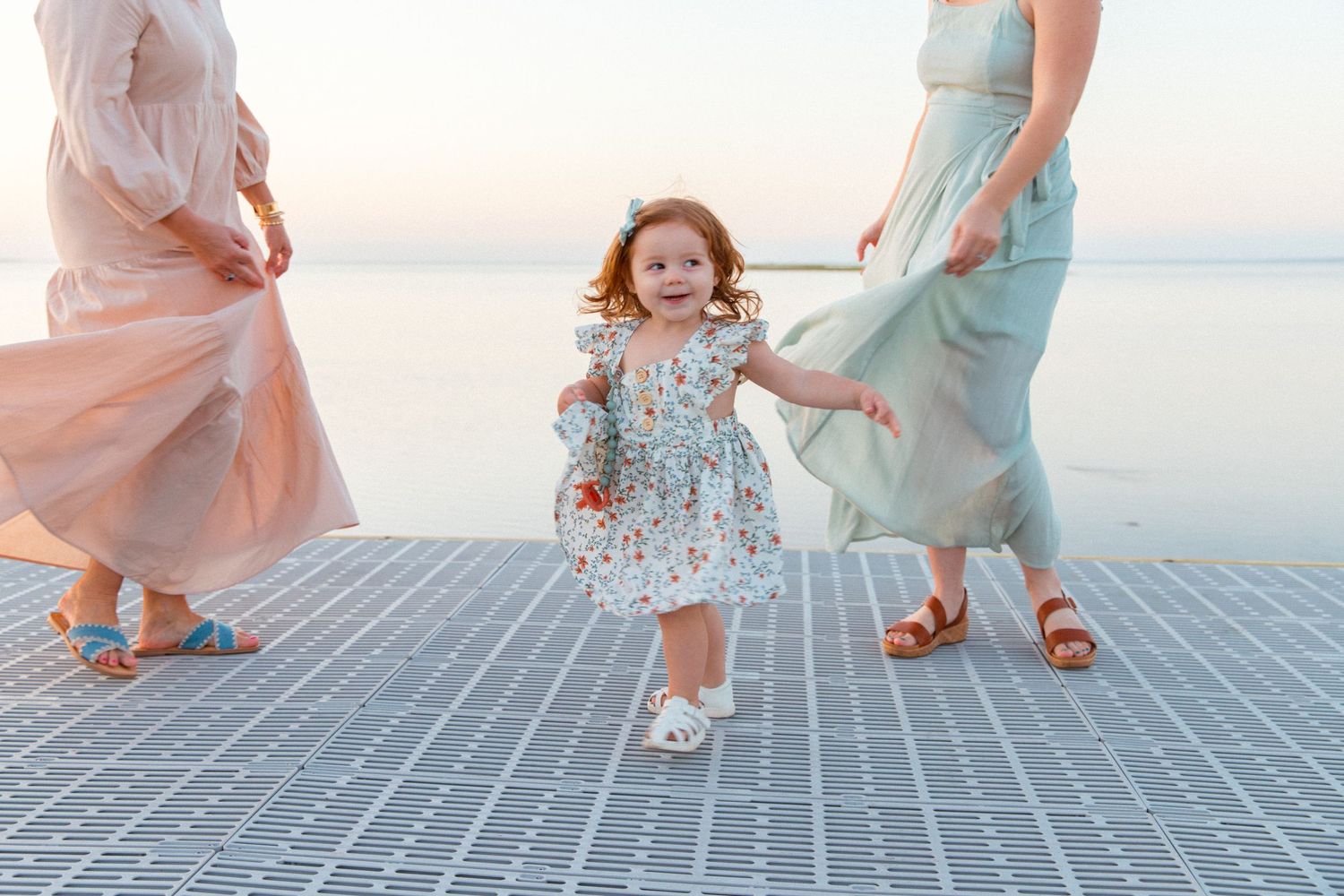 A child in a pink dress twirls and dances playfully on a gray tiled surface at sunset.