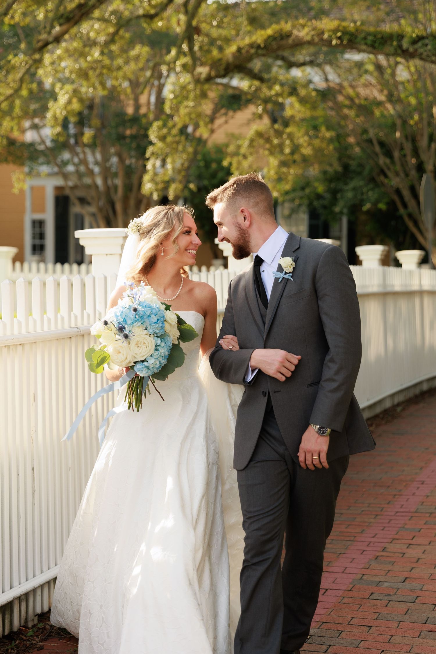 Wedding couple poses near a white picket fence with blooming yellow trees in the background.