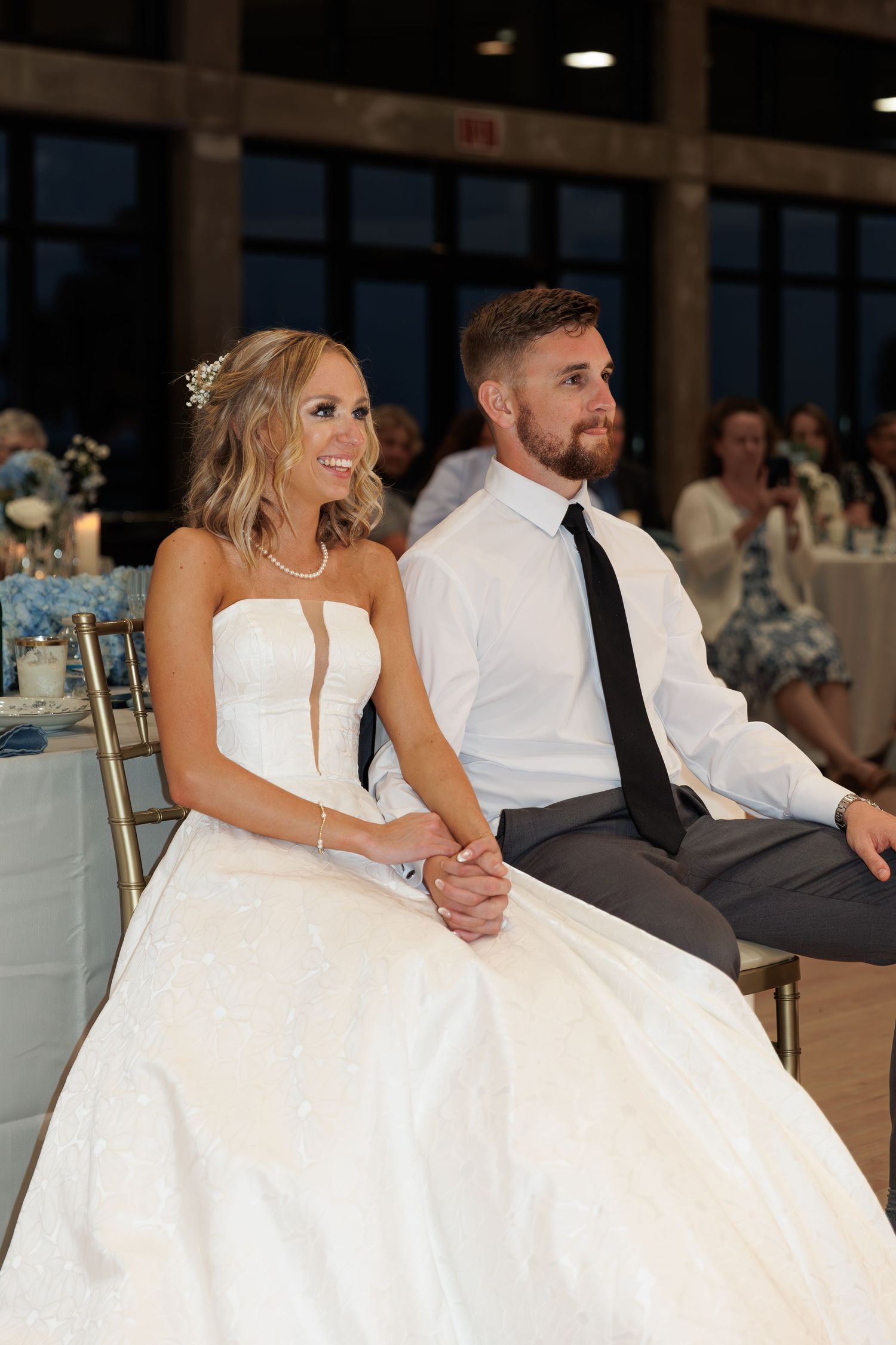 Newlyweds sitting together at their reception, bride in white gown and groom in white shirt.