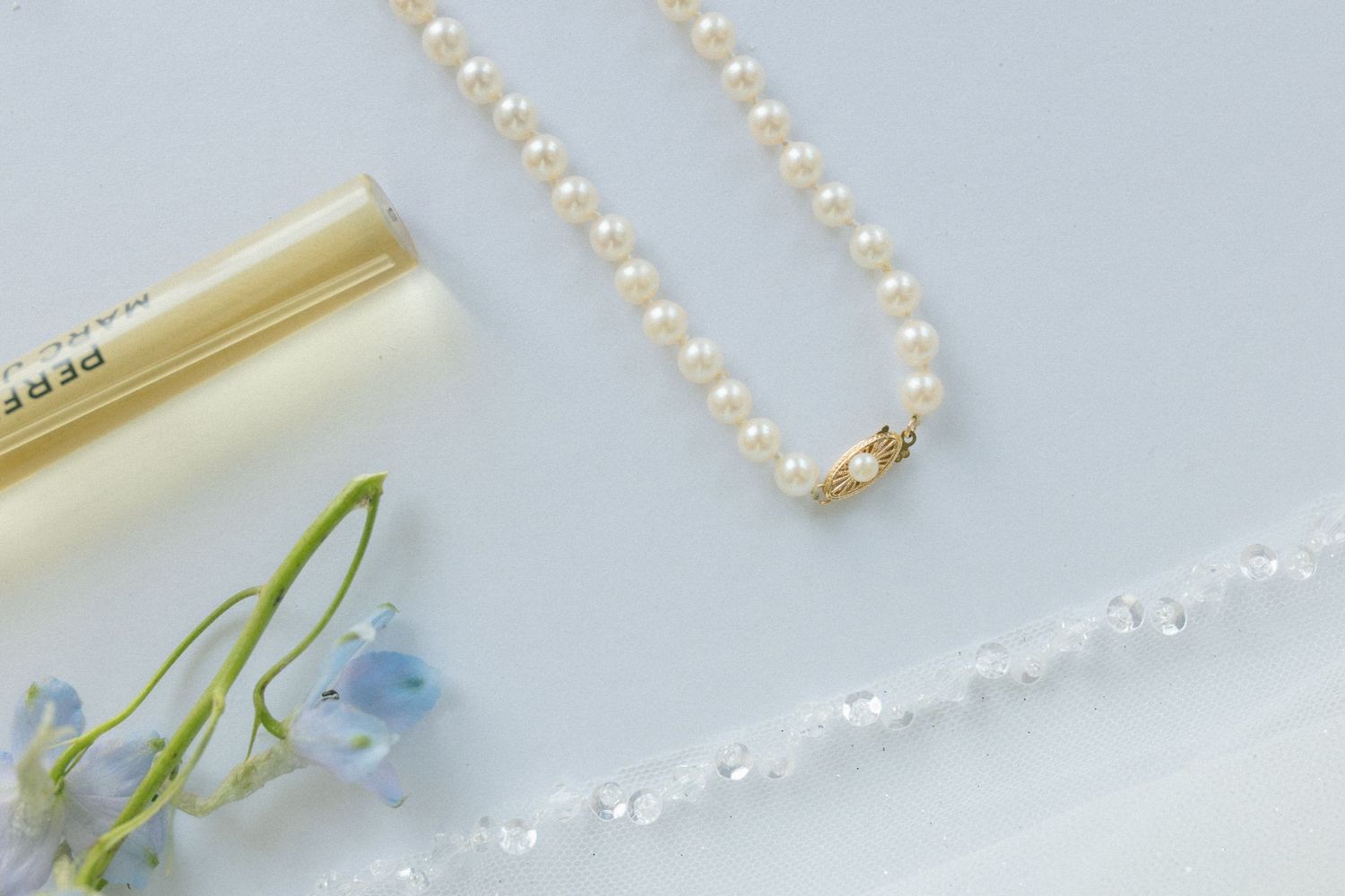 Elegant pearl necklace with blue flowers and gold accents on a light background.
