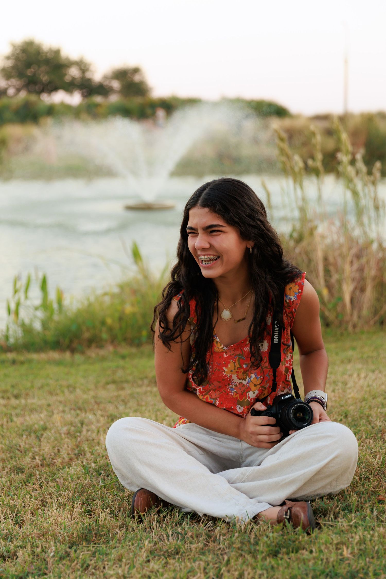 Camera enthusiast relaxes on lawn near decorative fountain during sunset photo session.