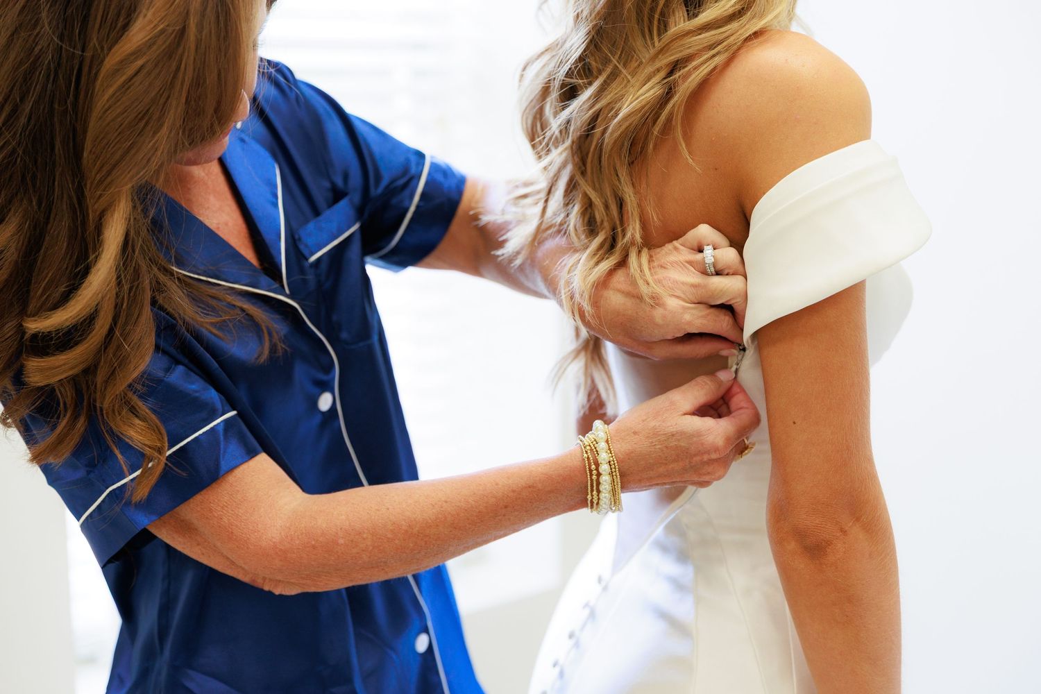 Healthcare professional in blue scrubs helps adjust a white off-shoulder garment during a medical appointment.