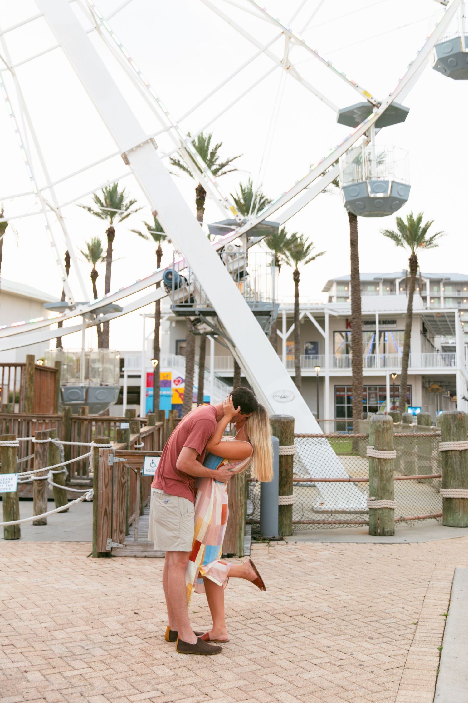 Couple sharing romantic kiss in front of a ferris wheel at an amusement park.