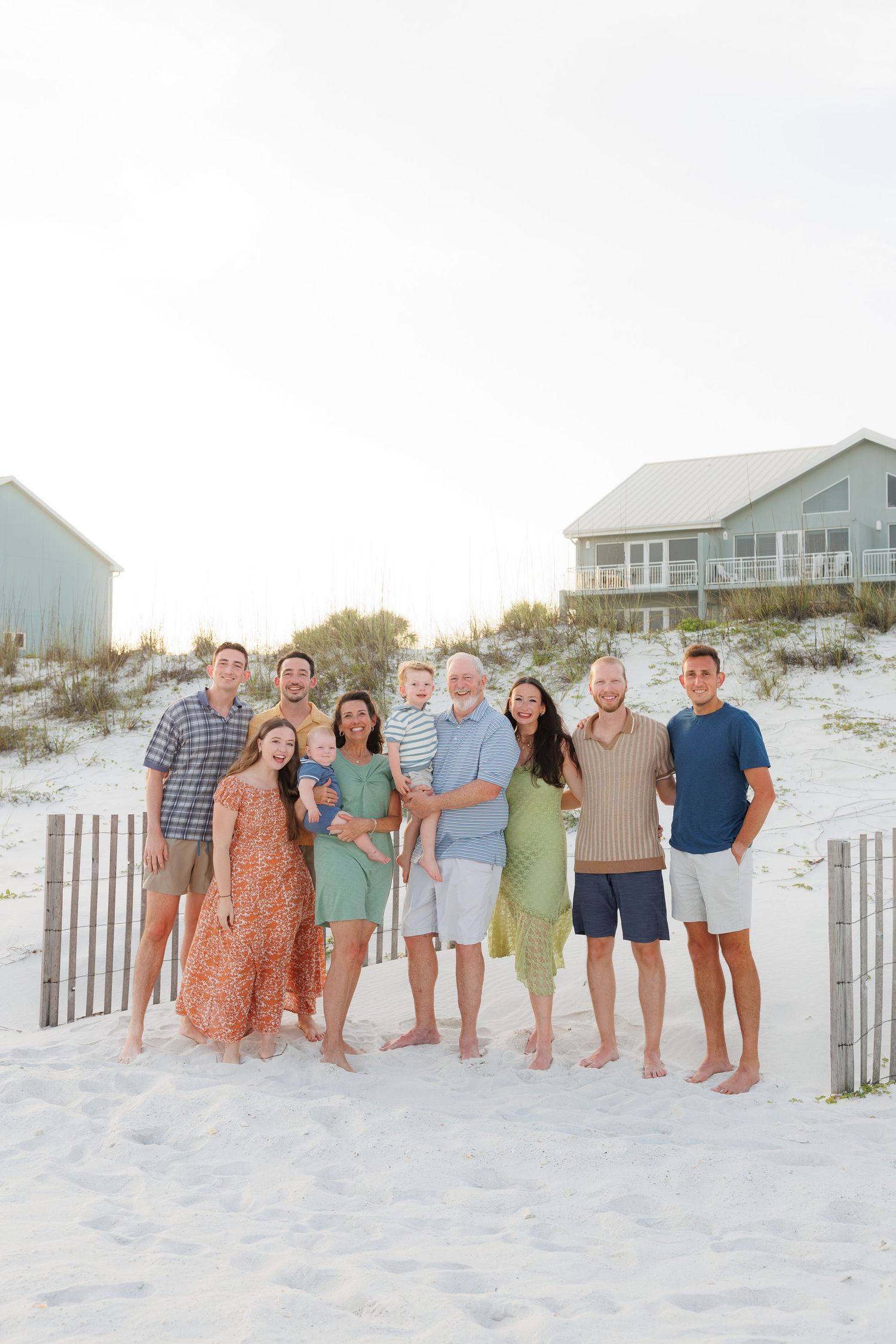 Large family group portrait on white sand beach with coastal homes in background.