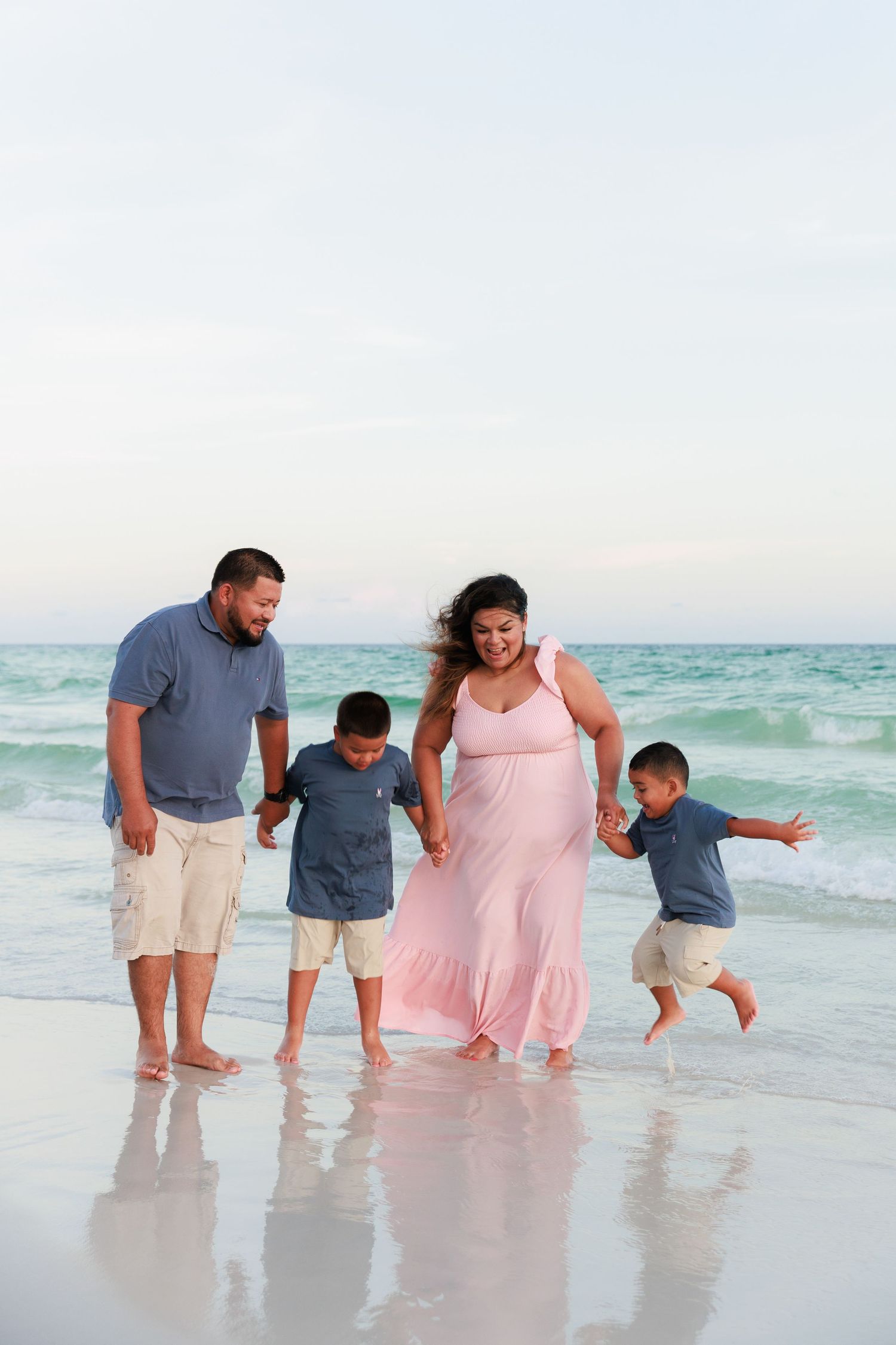 A family walks together holding hands along a beautiful beach with turquoise waves and white sand.