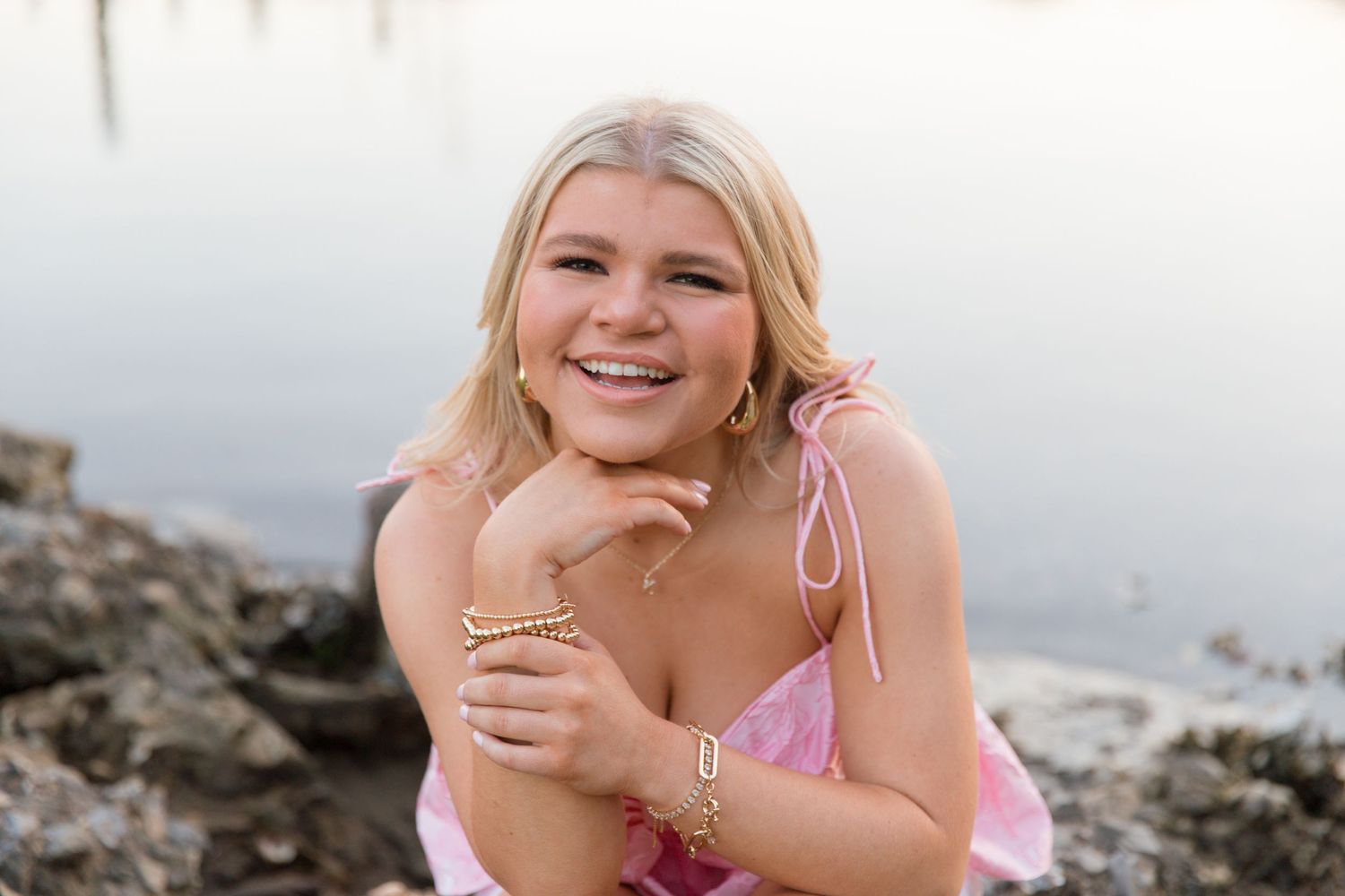 A person in a pink swimsuit poses on rocky beach terrain at sunset.