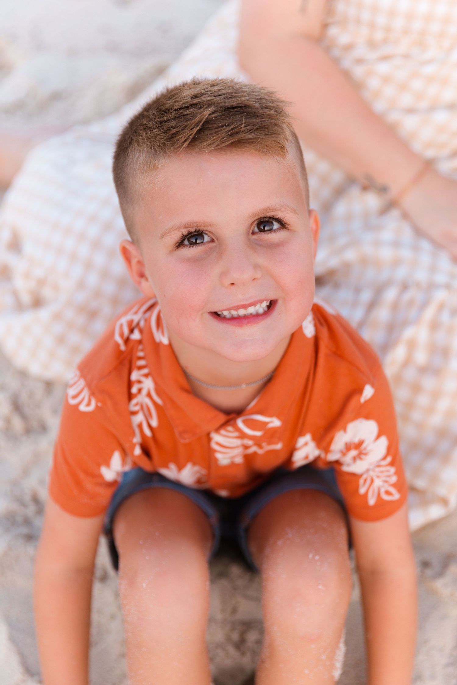 Child in orange t-shirt sitting on textured surface with bright smile and playful expression.
