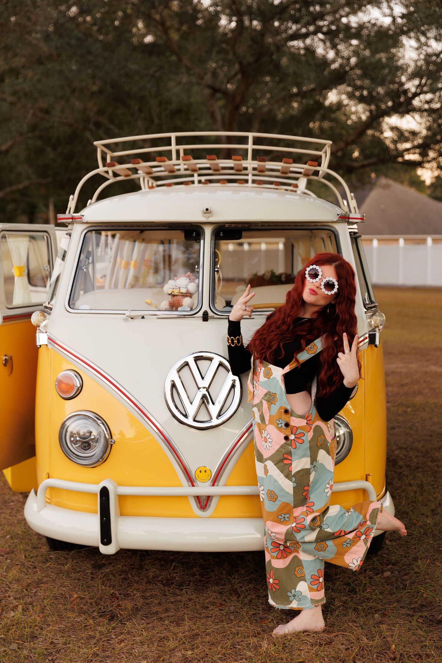 A yellow and white vintage Volkswagen bus parked on grass during golden hour with people sitting in its open doorway.